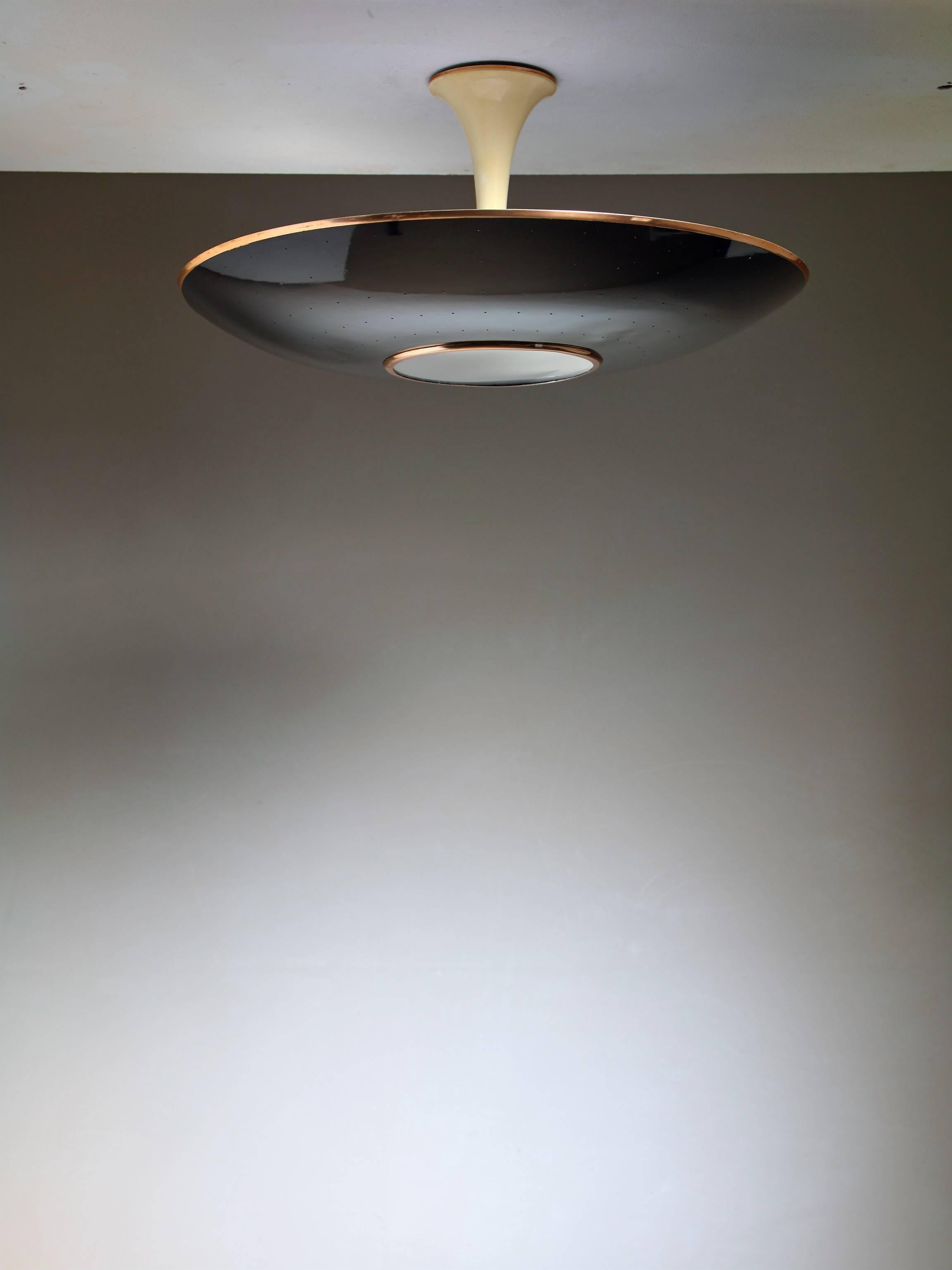 A Mid-Century ceiling lamp with a curved black lacquered metal shade with a frosted glass diffuser in the centre. The lamp has three E27 light bulbs and the shade has pin point perforations.