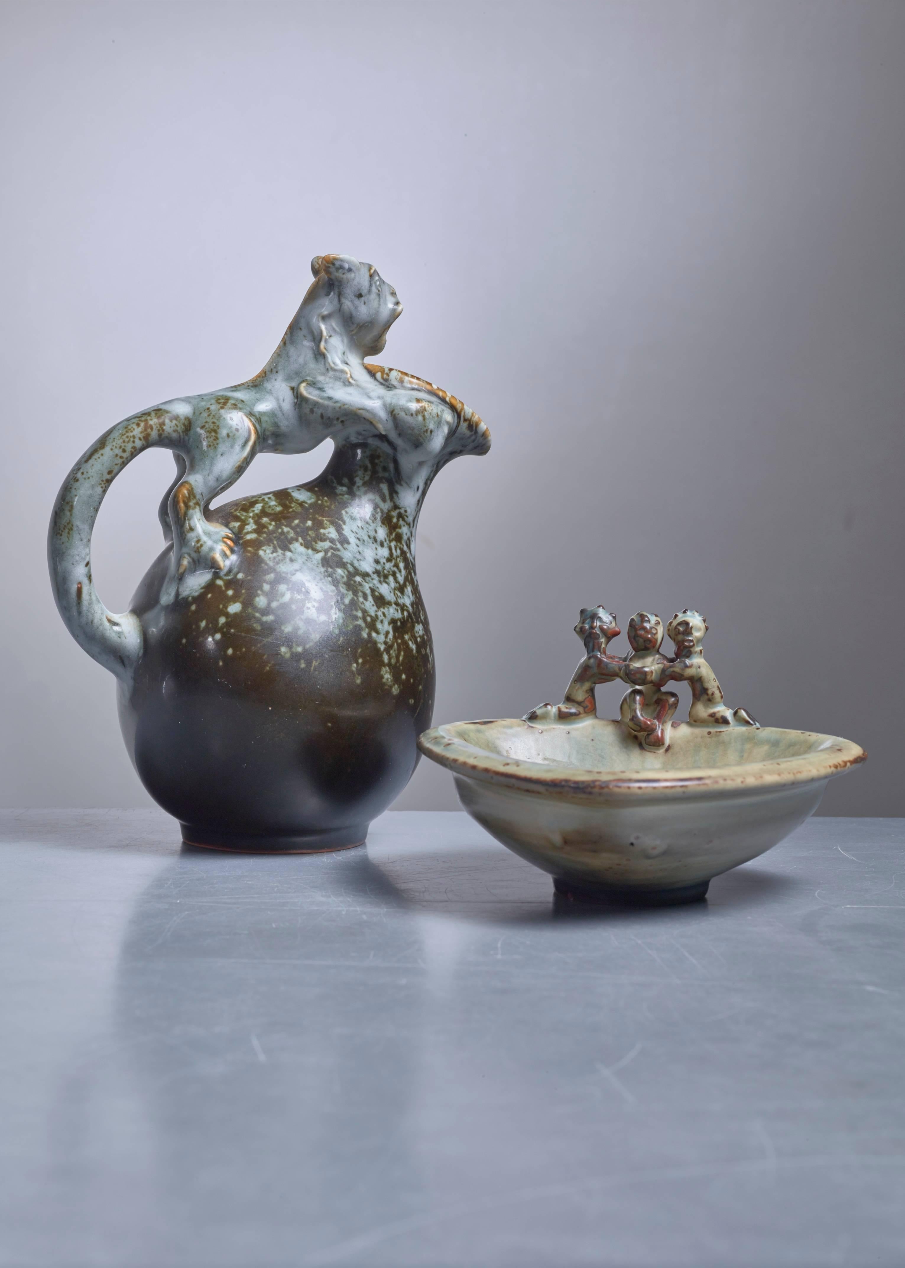 A stoneware set by Bode Willumsen for Royal Copenhagen. The jug has a lynx as a handle. The triangular ashtray or bowl has three figures sitting on the rim.
The height of the pieces is 21 (8.3 inch) and 10 cm (4 inch). Signed with monogram

Bode