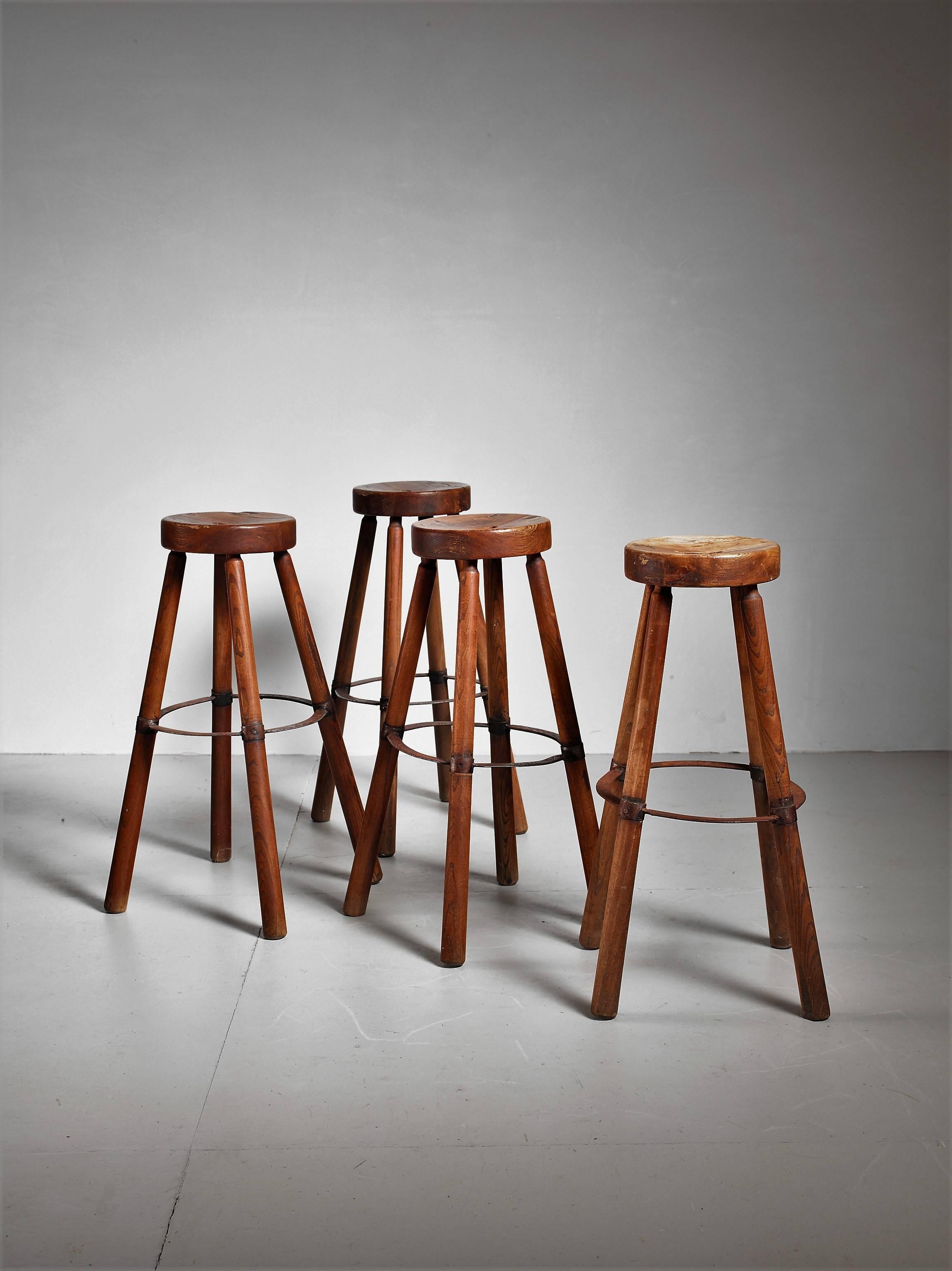 A set of four modernist French high stools in the manner of Pierre Jeanneret, made of teak with a metal foot ring. The thick top has a diameter of 27 cm (10.5 inch) and has a slot in it. These pieces have a sturdy, Industrial look and has a great
