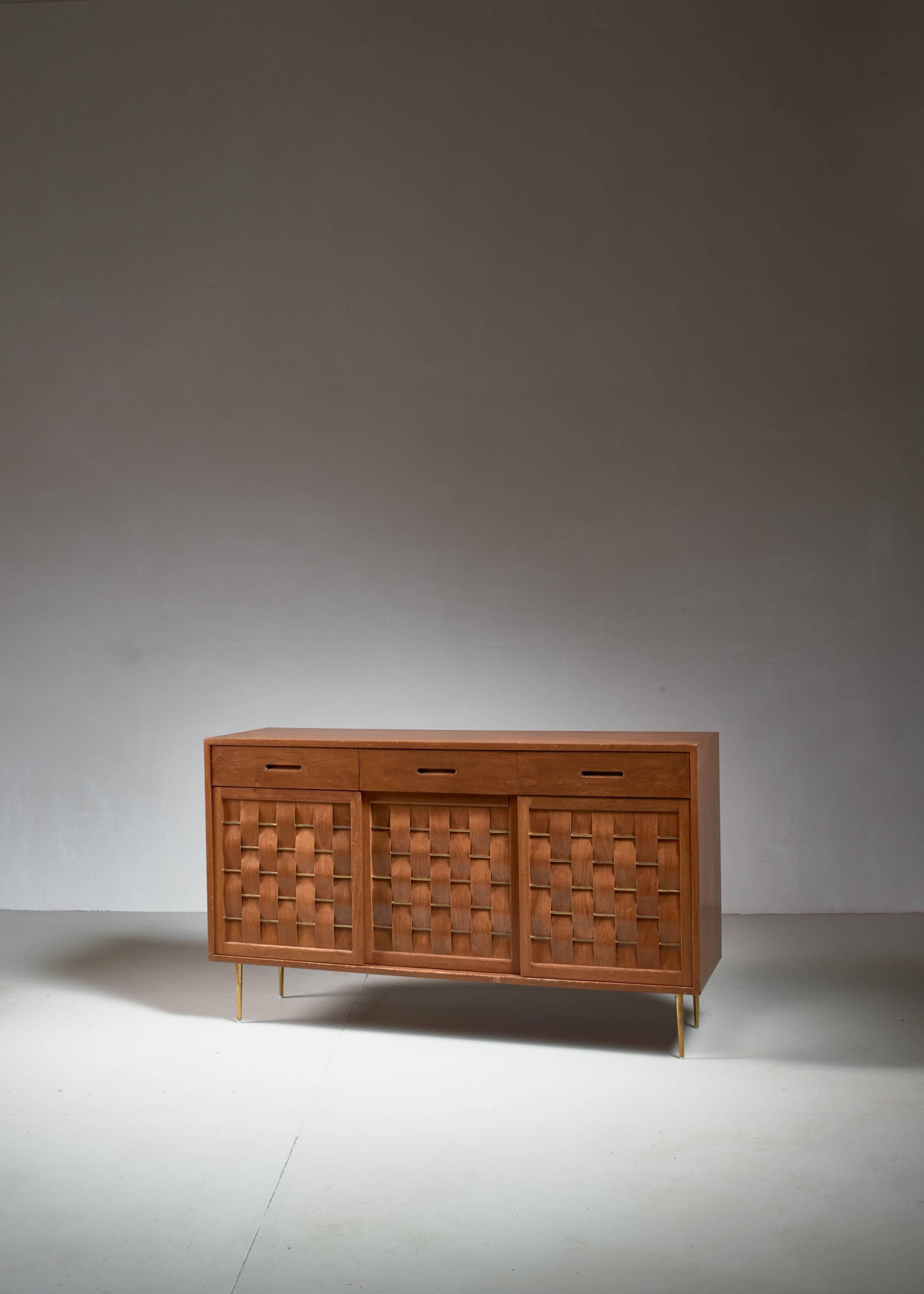 A rare and wonderful condition Edward Wormley wooden credenza for Dunbar, a rare edition with elegant brass feet.
It has three sliding panel doors and three drawers above them. The doors are made of thin wooden strips woven through brass rods, with