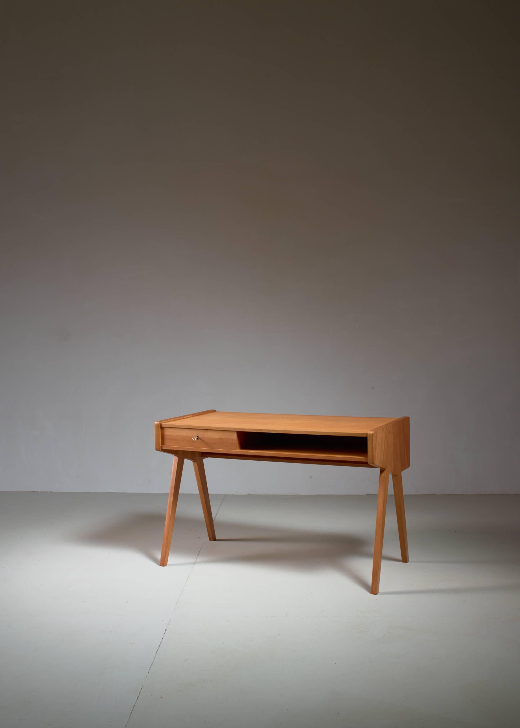 A small wooden writing or ladies desk on V-shaped legs by German designer Helmut Magg for WK Möbel. The desk has drawer and storage space in front and a shallow storage space at the back. The leg height is 61 cm (24