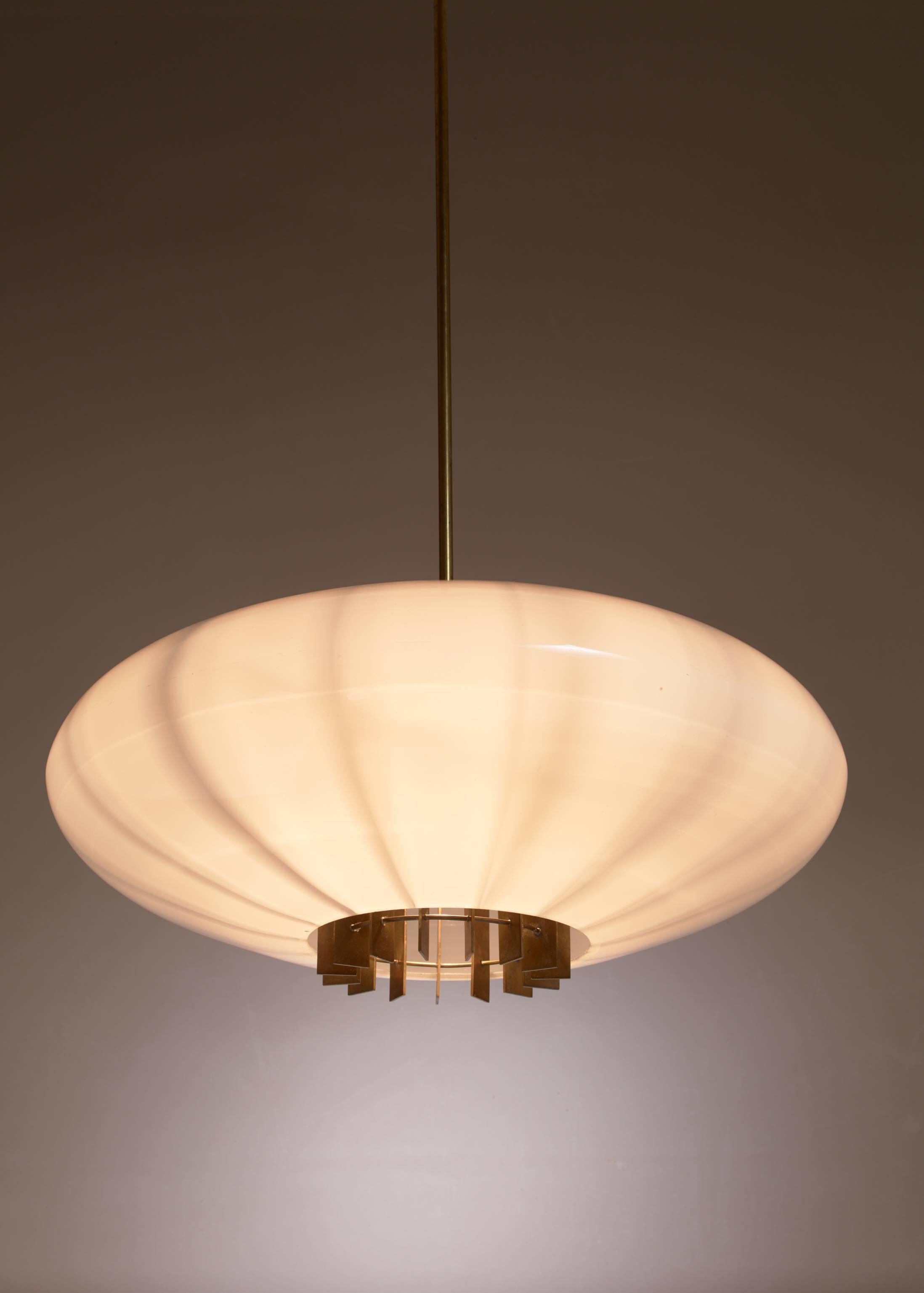 One of two large Swedish, pill-shaped opaline glass pendant lamps with a brass grid inside and a brass stem.

        