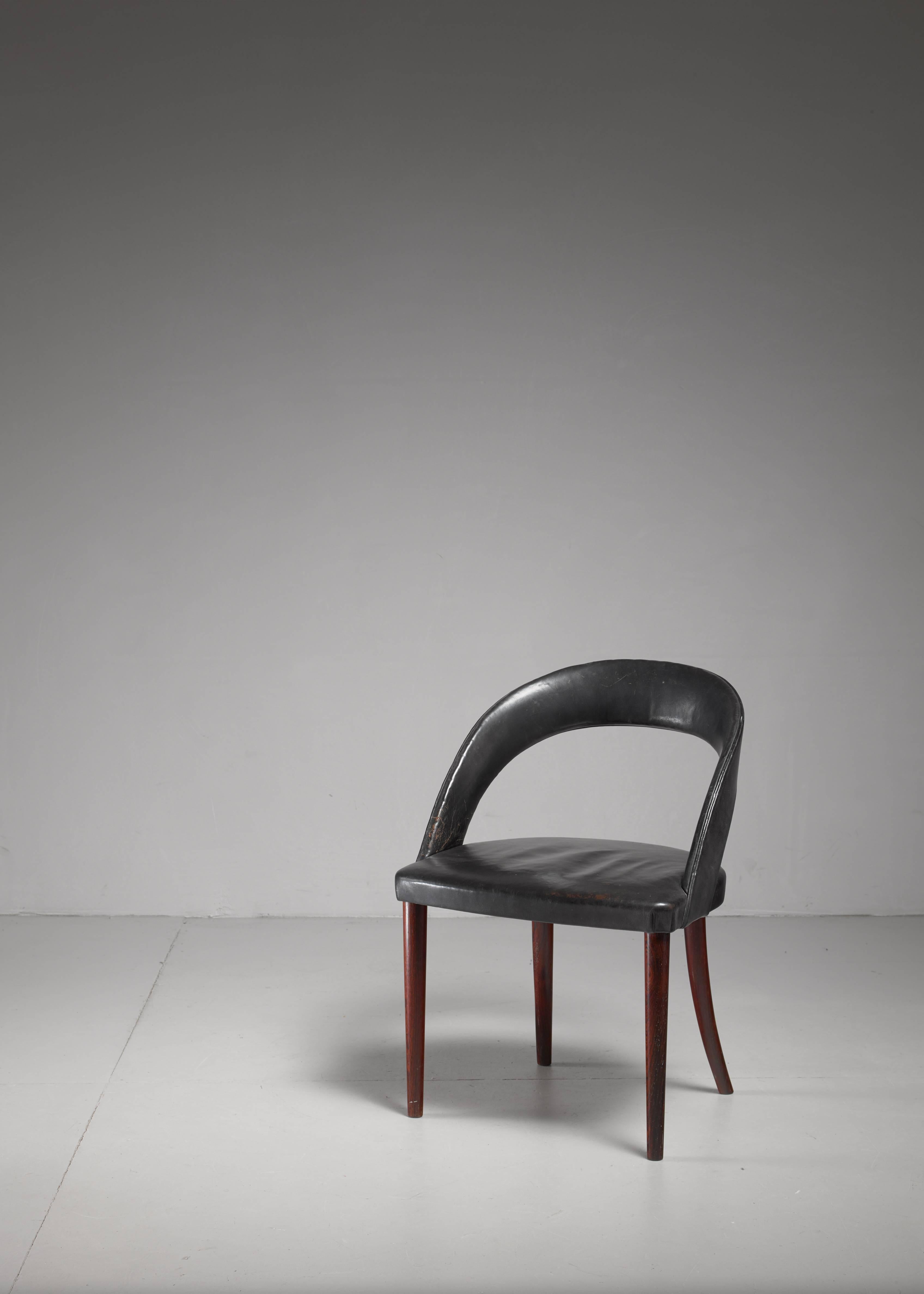 An elegant vanity chair by Danish designer Frode Holm for Illums Bolighus. The chair stands on round, tapering rosewood legs and has a thin and curved backrest. The seat and back are upholstered with black leather. The leather has a mild wear, which