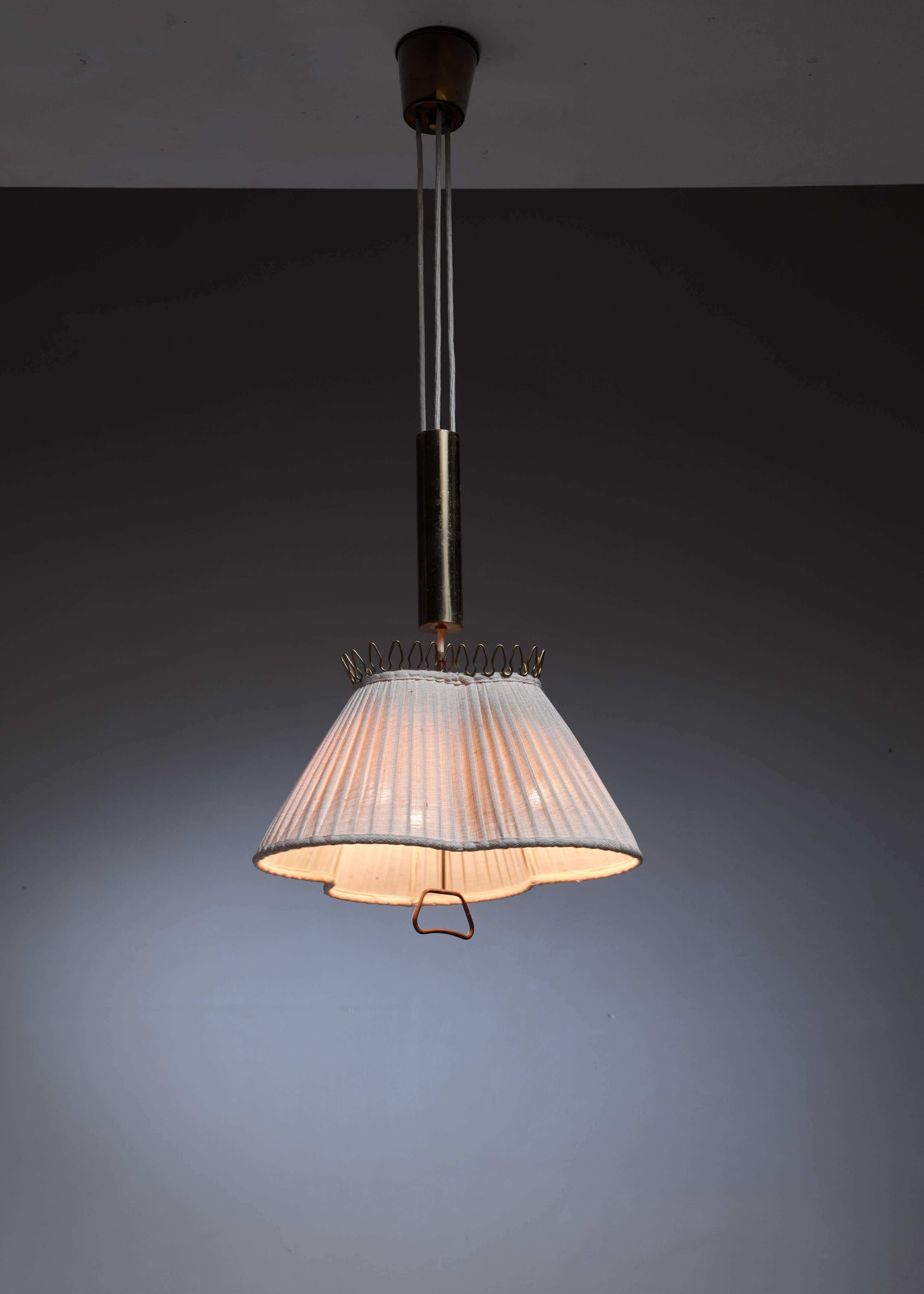 A 1940s pendant lamp from Sweden. The pleated fabric shade has a remarkable trefoil shape with a brass crown-like decoration op top and a subtle brass pull. The height of the lamp is adjustable (between circa 100 and 180 cm) with the beautiful