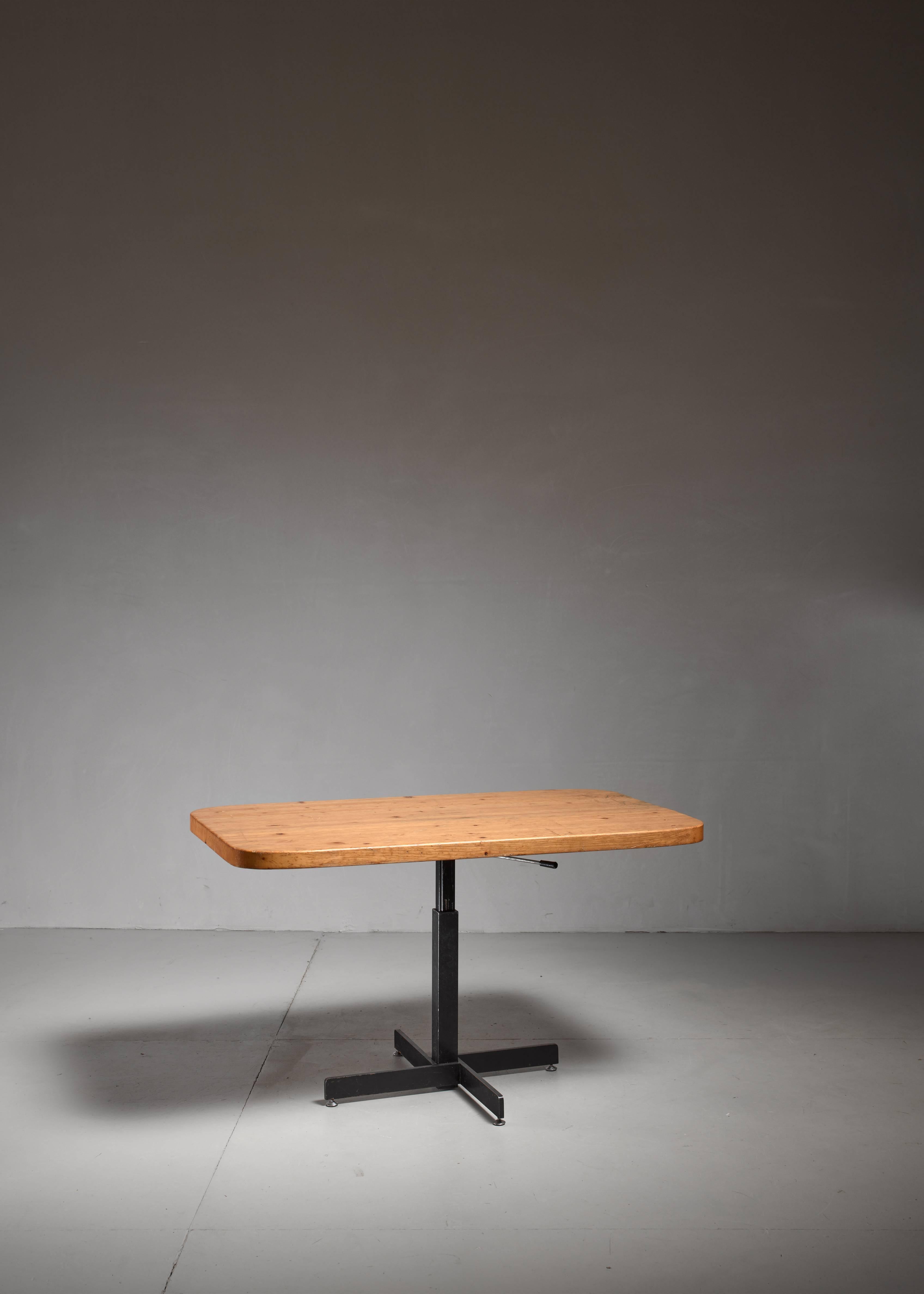 An early adjustable dining table by Charlotte Perriand, made of pine with black a black metal base. The height can vary between 52 and 71 cm.
The top has sawtooth connections and has beautifully aged from extensive usage.

The table was designed for