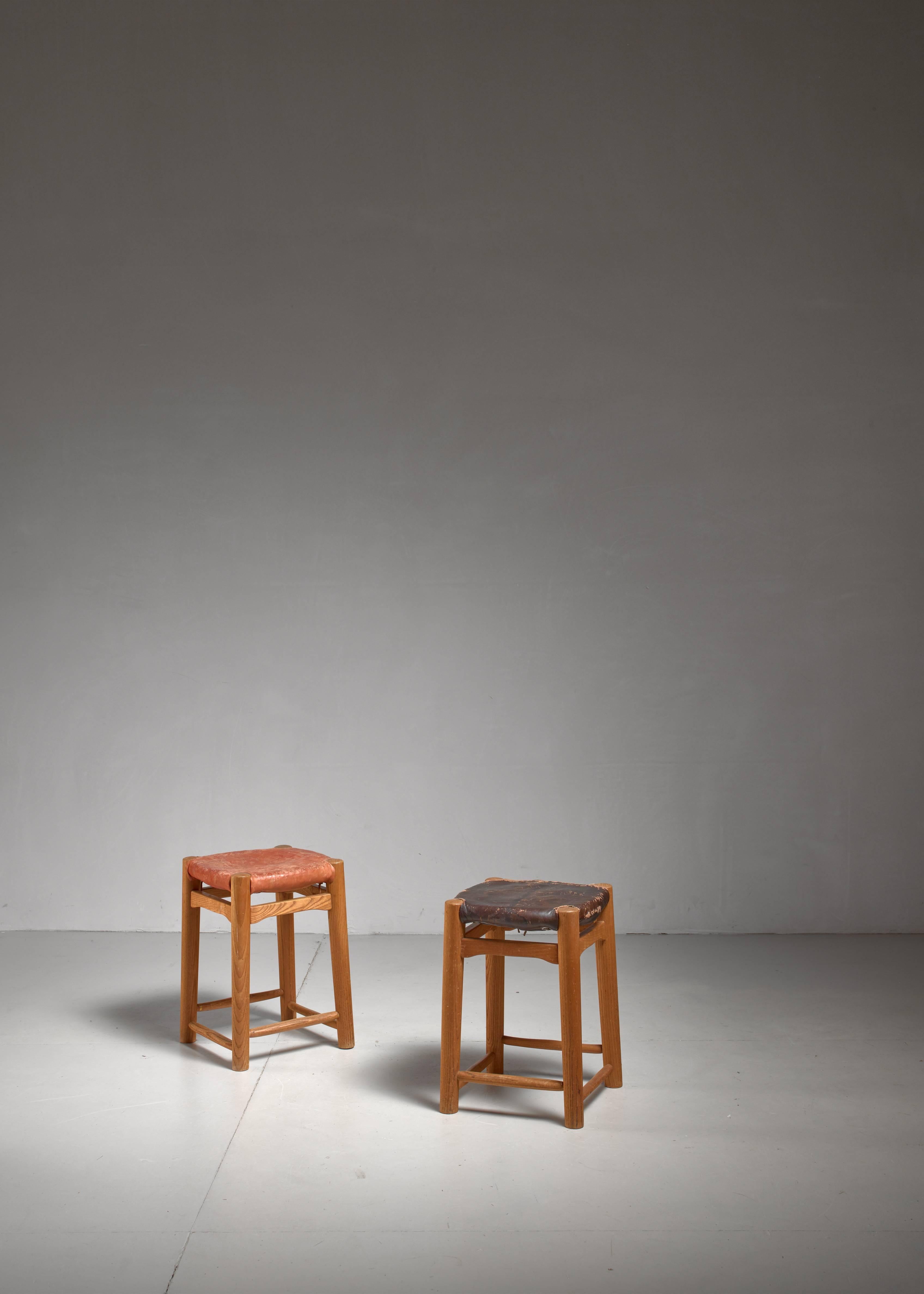 A pair of French stools with an oak frame, rush seat and a red and a brown leather seat pad, reminiscent to the work of Charlotte Perriand.