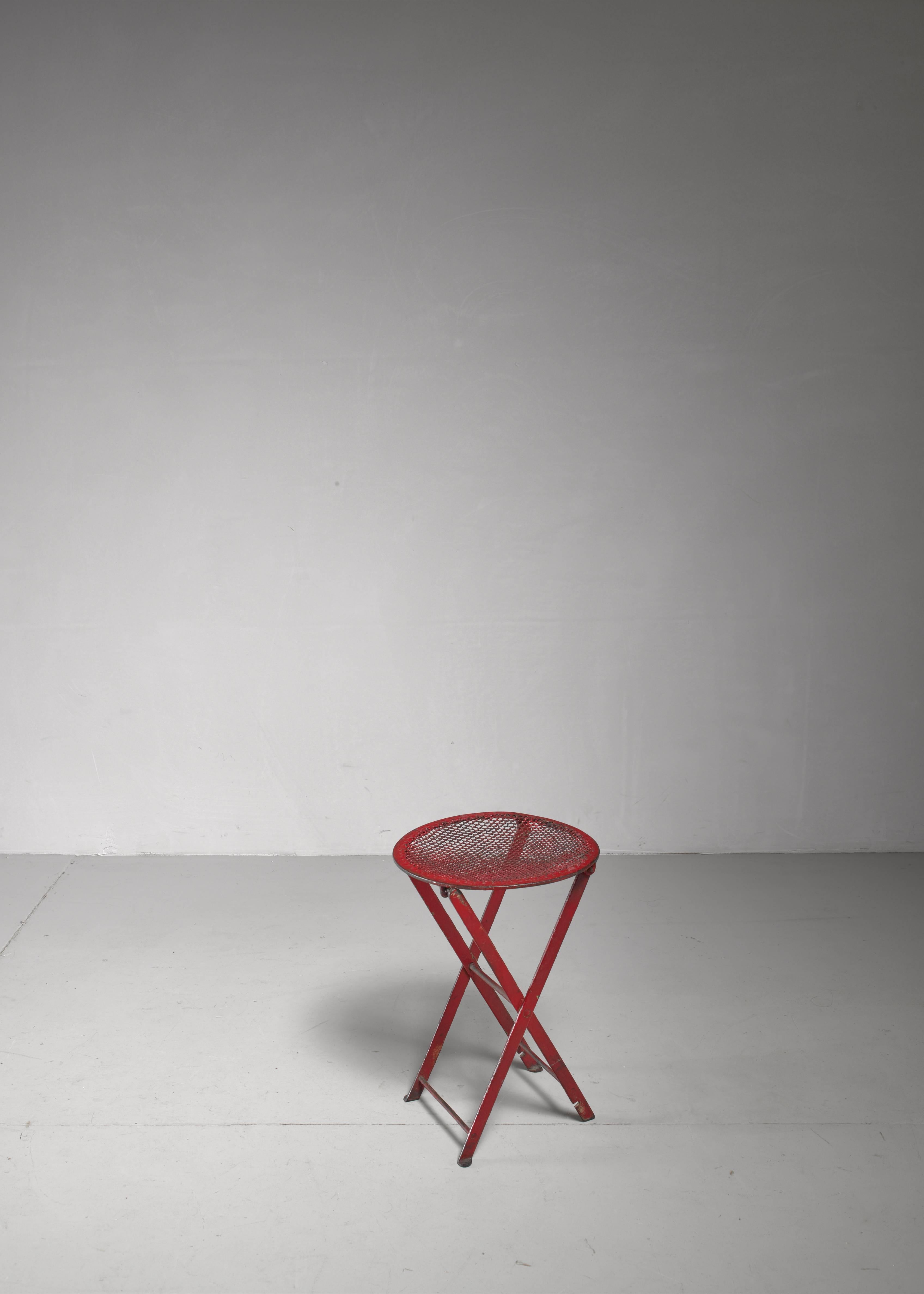A foldable stool made of red metal and a mesh metal seating. Great for outdoor use and/or as side or plant table. 