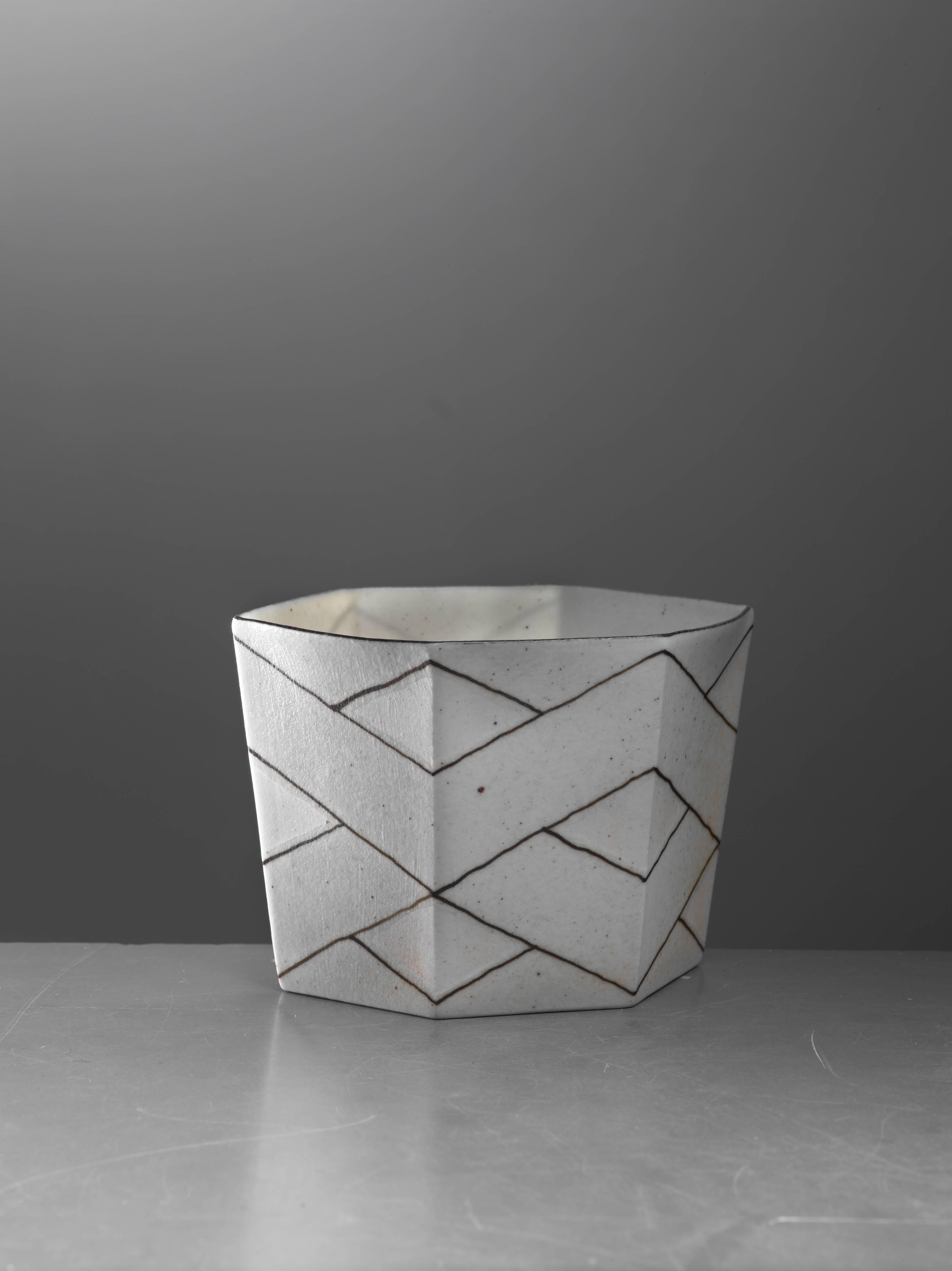 A small, hexagonal porcelain bowl by Danish ceramist Bodil Manz (1943). The bowl is decorated with a geometric pattern, mostly off-white with light pink parts. It is a wonderful sample of the thin, translucent porcelain pieces Bodil Manz is known