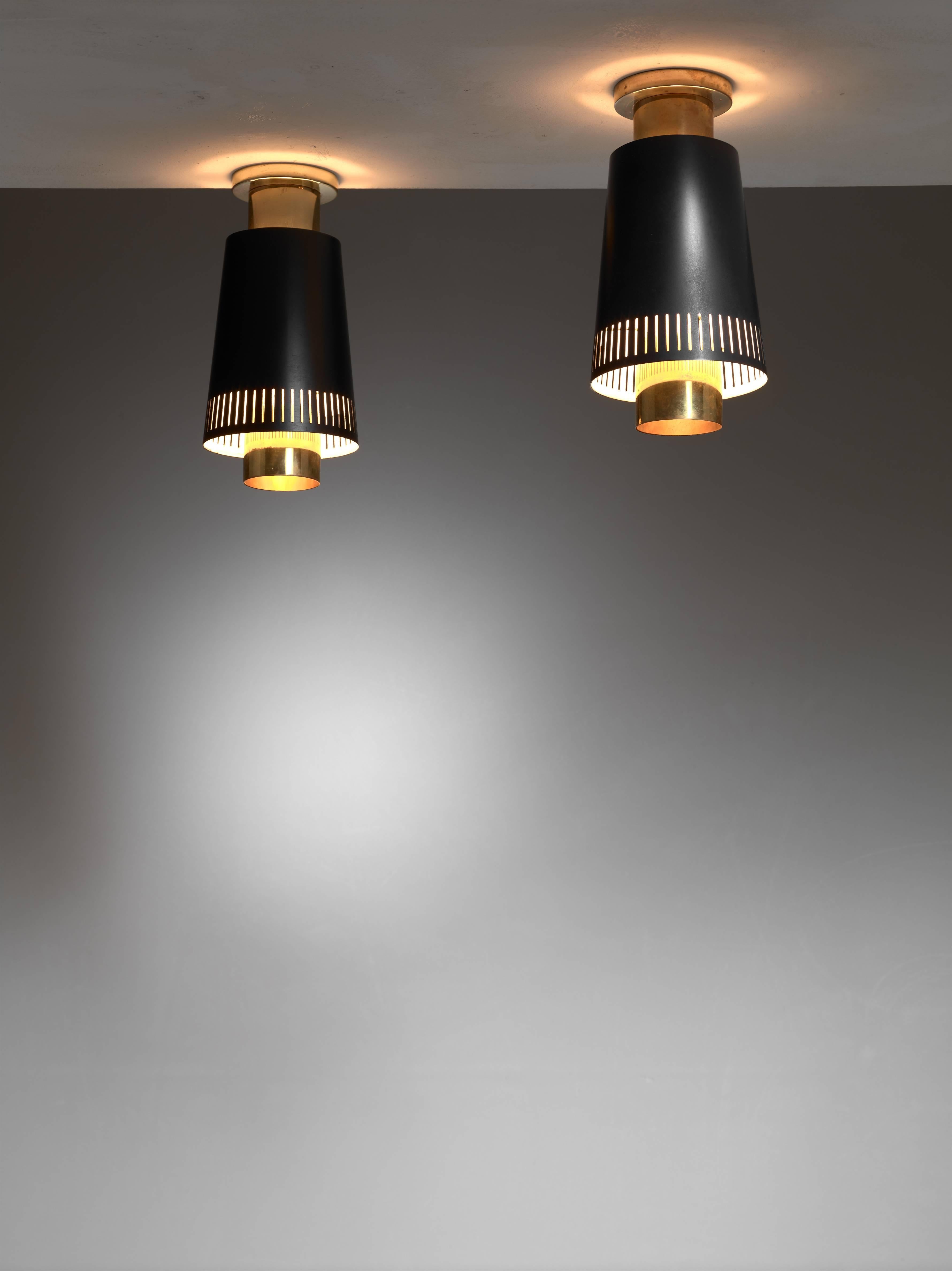 A pair of Paavo Tynell model 9067 ceiling lamps for Taito, Finland. The lamps have a shade of black lacquered aluminum with vertical perforations and a brass diffuser and ceiling mount. One of the lamps is marked by Taito and both are in an