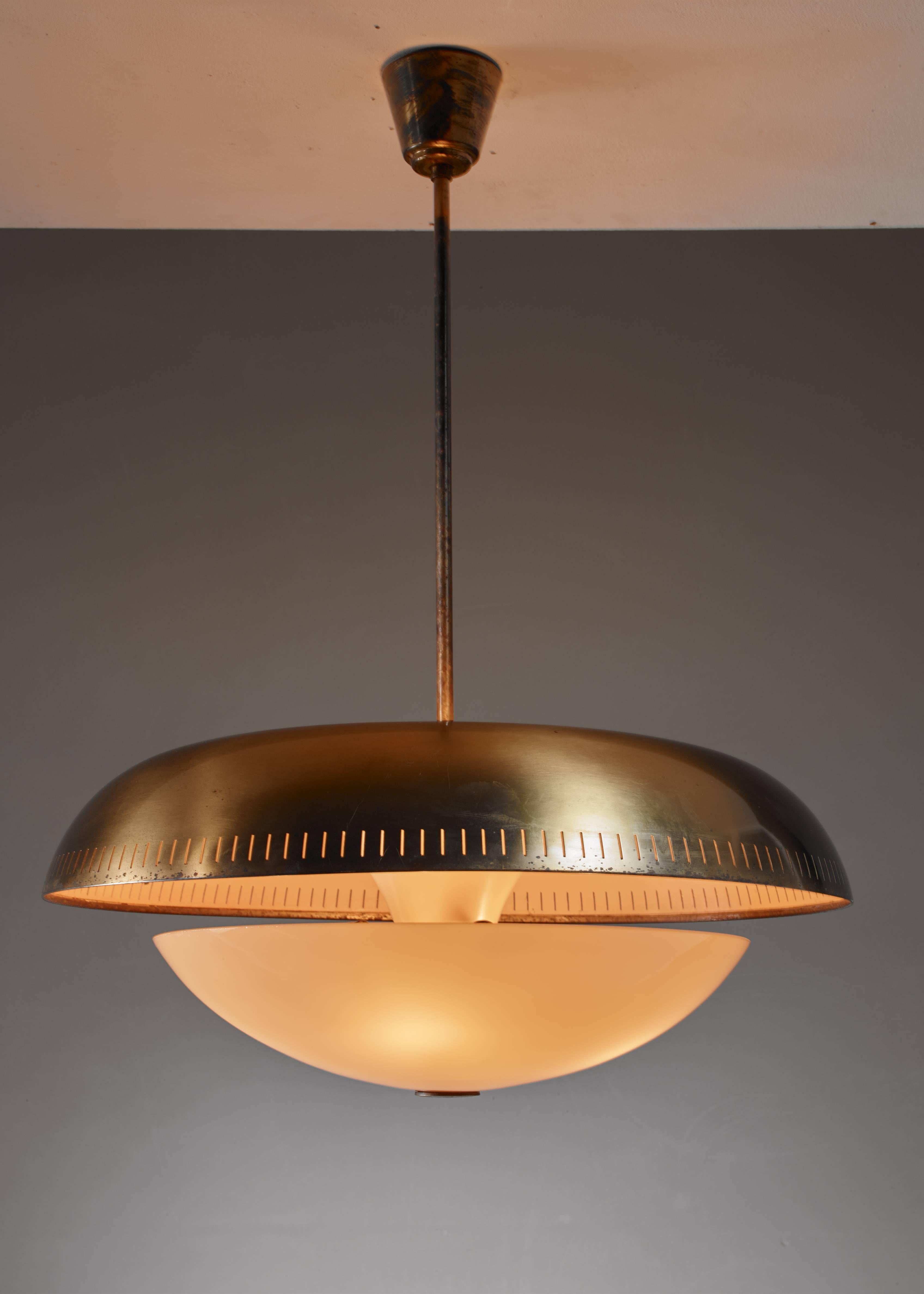A Harald Notini pendant lamp for Bohlmarks, made of a perforated brass shade with a yellow glass diffuser underneath. The combination of the yellow of the inside of the shade and the diffuser gives a beautiful warm light. The lamp has four light