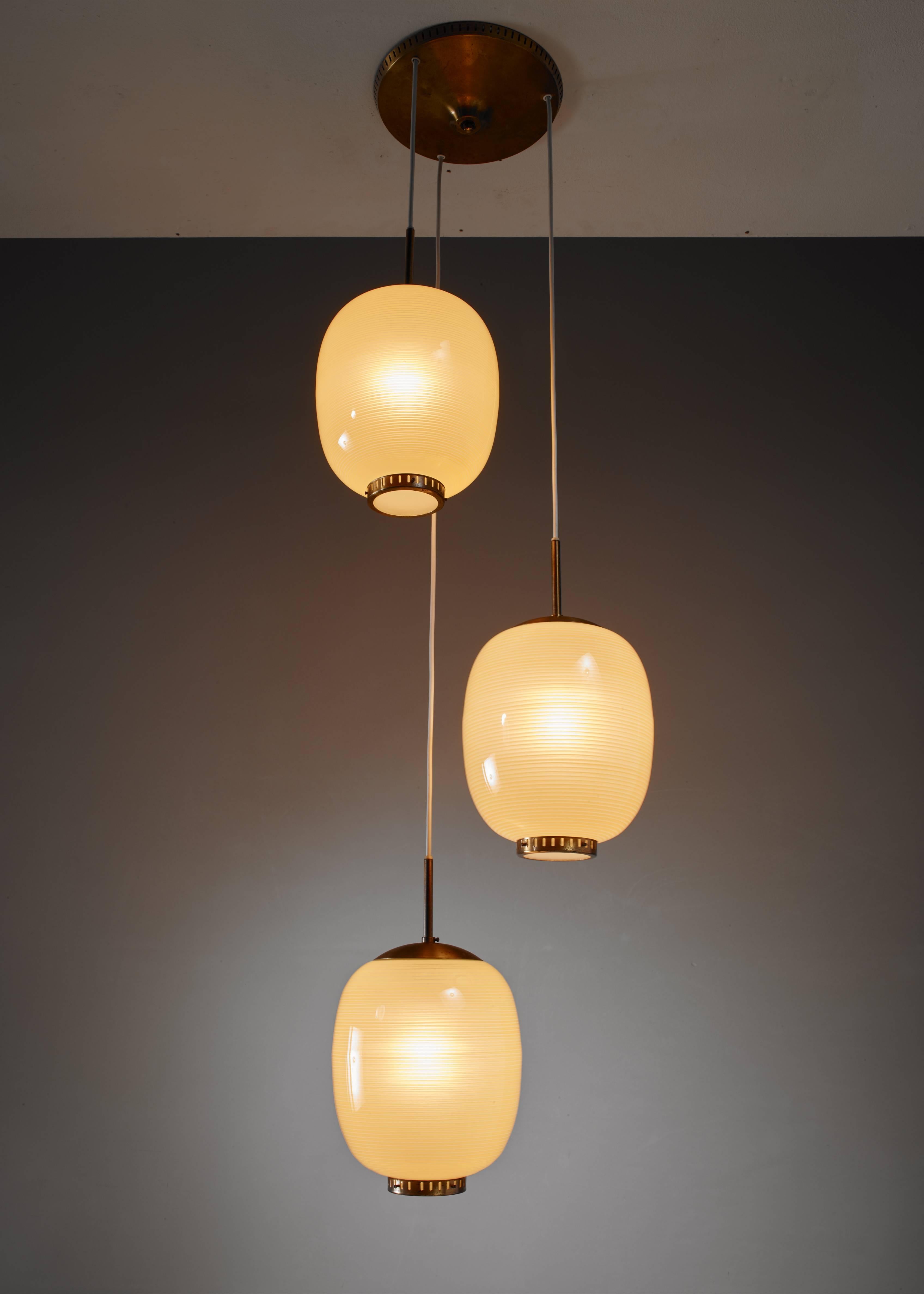 A chandelier with three pendant lamps by Danish designer Bent Karlby. The lamps are made of yellow glass with a striped pattern and hang from a brass canopy. The lamps have a brass ring with a frosted glass diffuser underneath.
The measurements