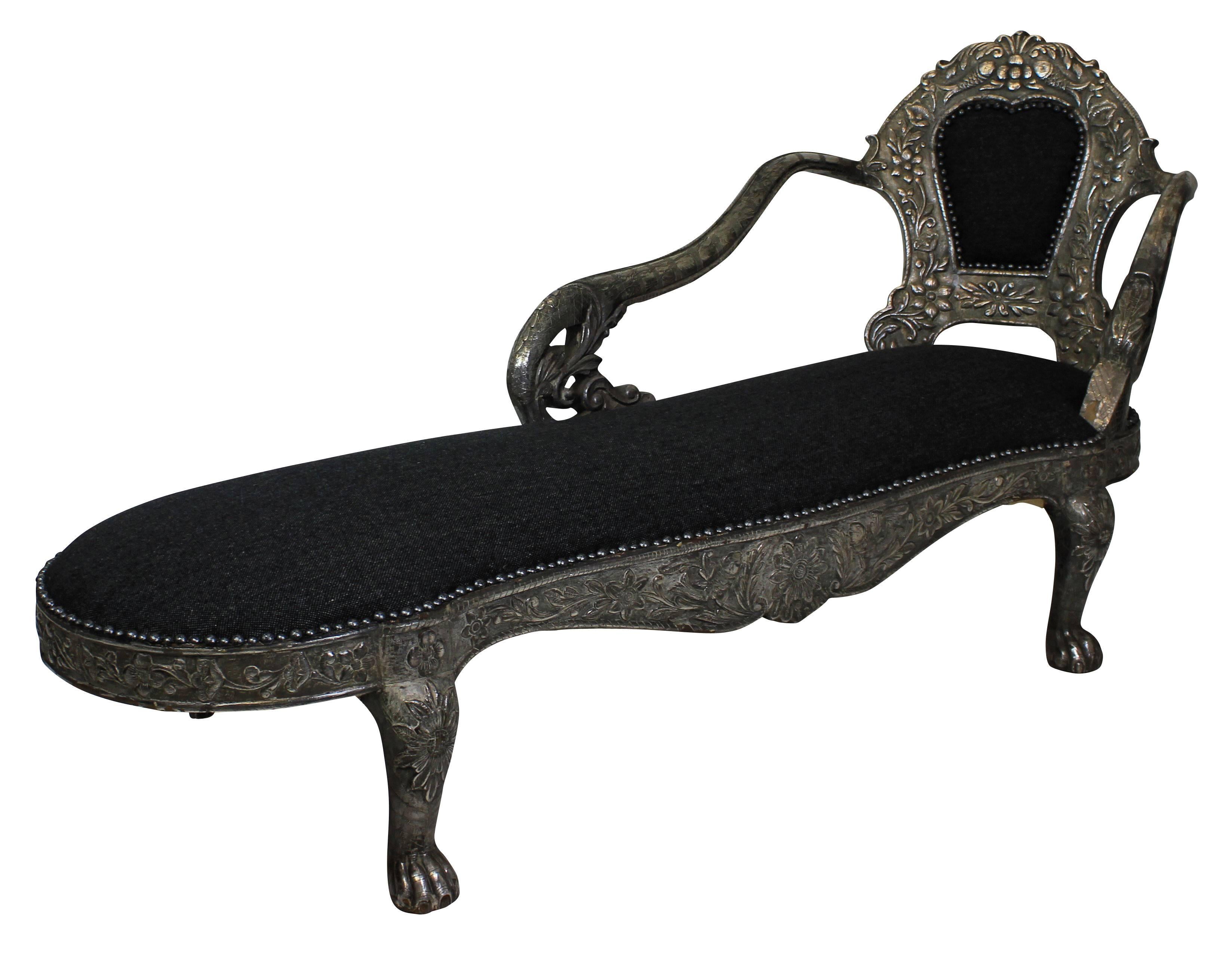 A fine Indian daybed in carved teak and covered in repousse silver depicting animals, birds and foliage on lion paw feet. Upholstered in grey wool and studded.