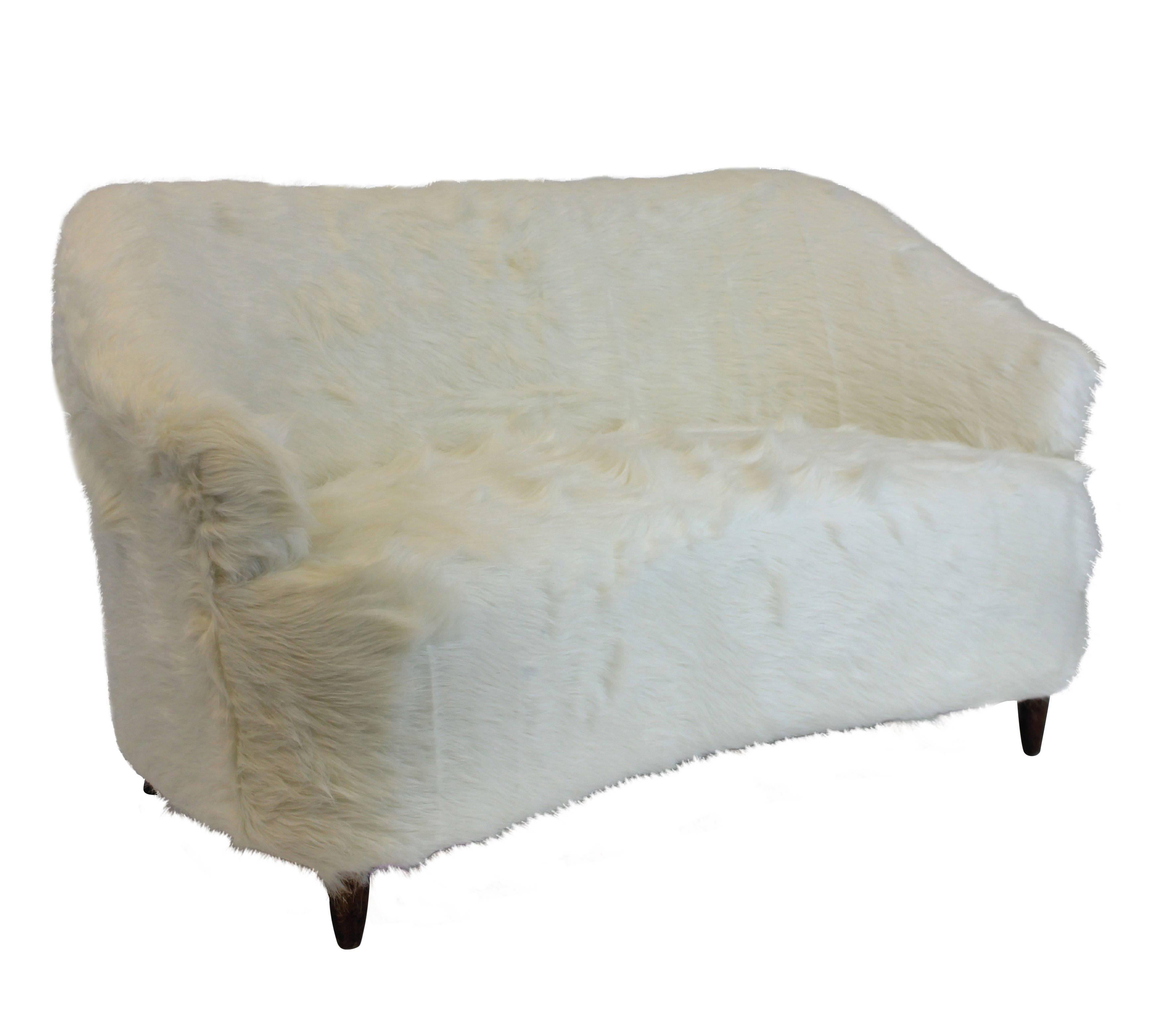 A cute Danish two-seat sofa in white imitation fur, of sculptural form, on turned legs.
   