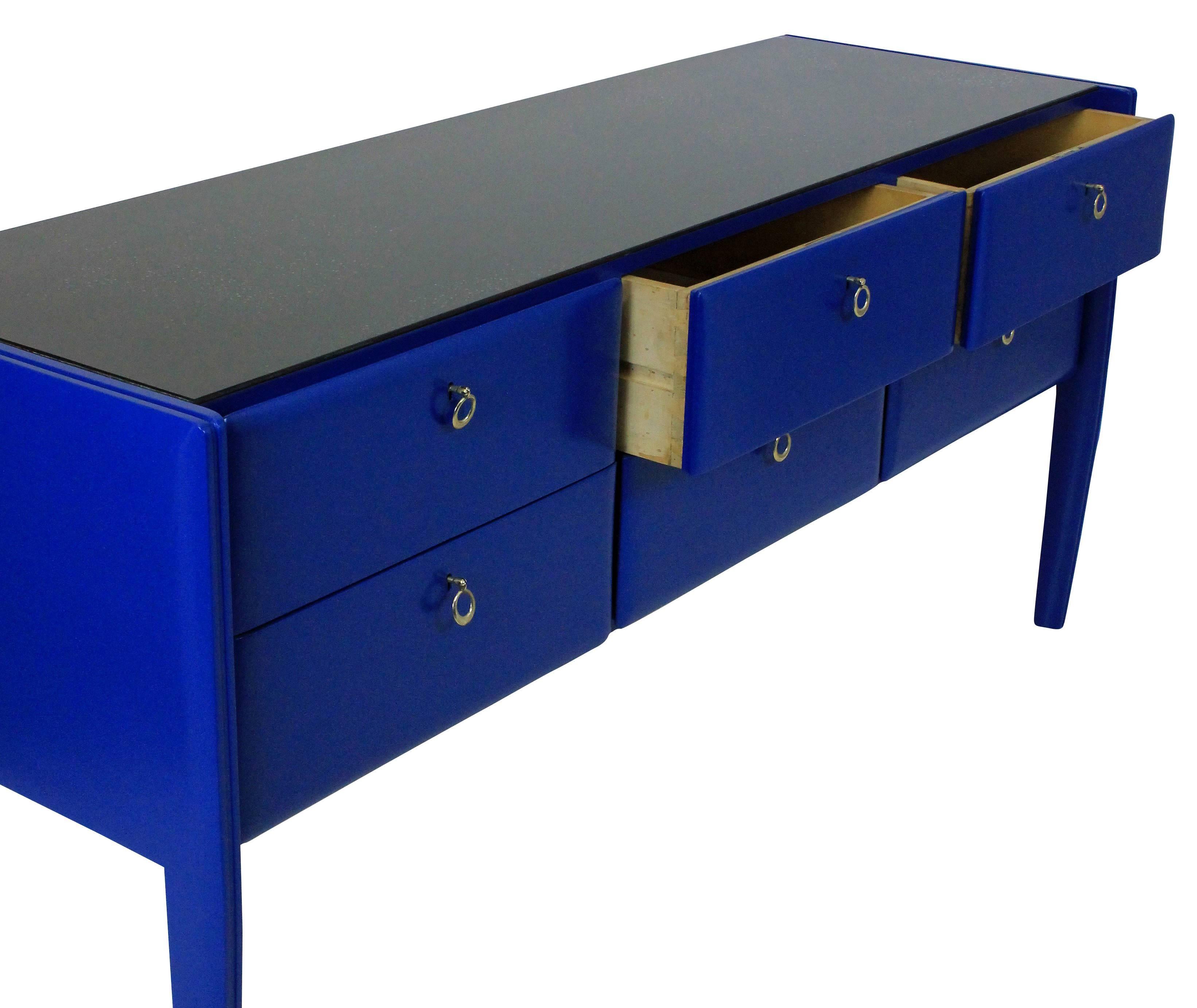 A stunning Italian midcentury credenza in cobalt blue lacquer. With six drawers, each with their own brass key pull and the darker blue glass top.

  