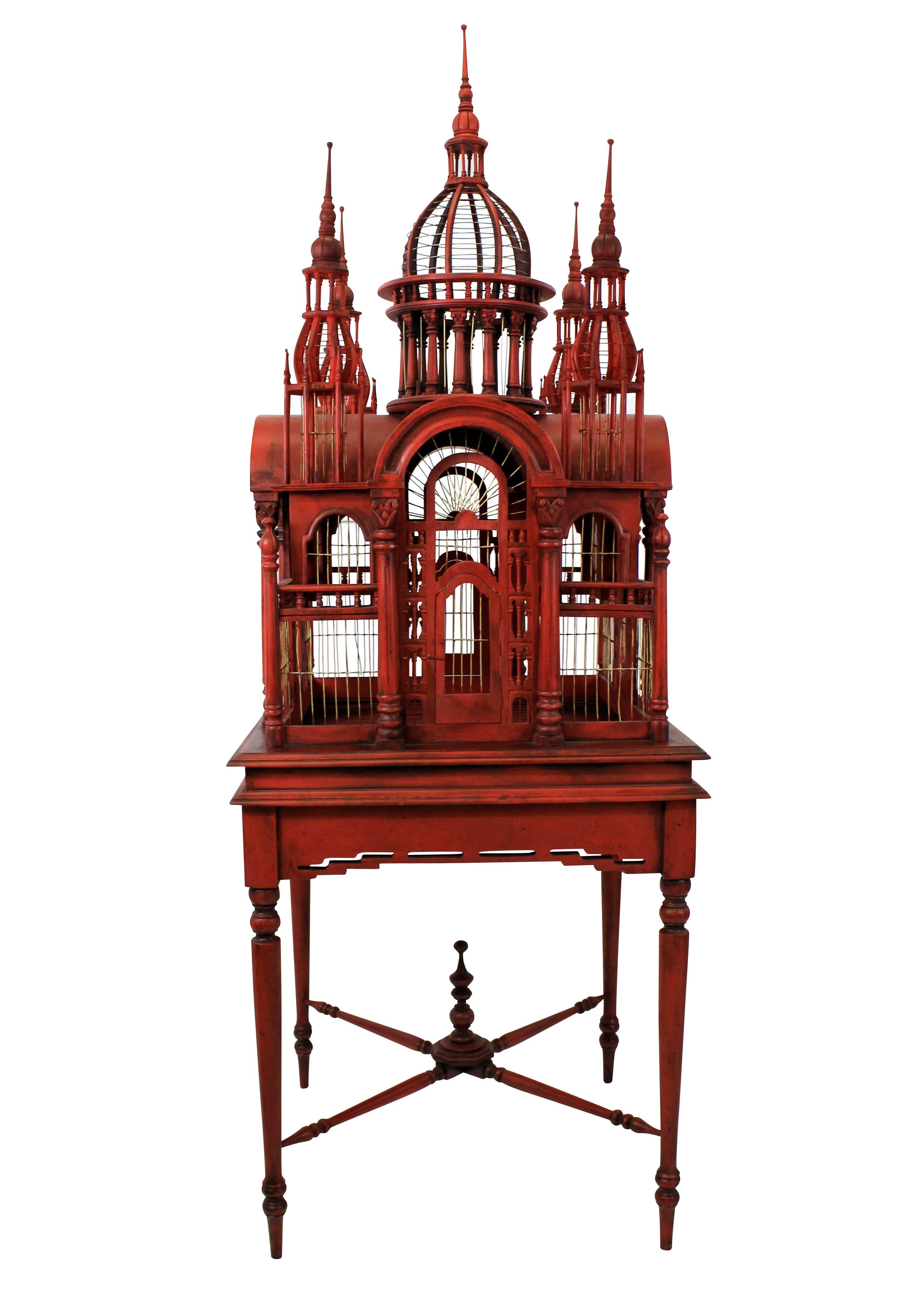 A pair of large and impressive wooden aviaries in red lacquer in the form of Cathedrals. Each on a stand, with four doors and a tray bottom.