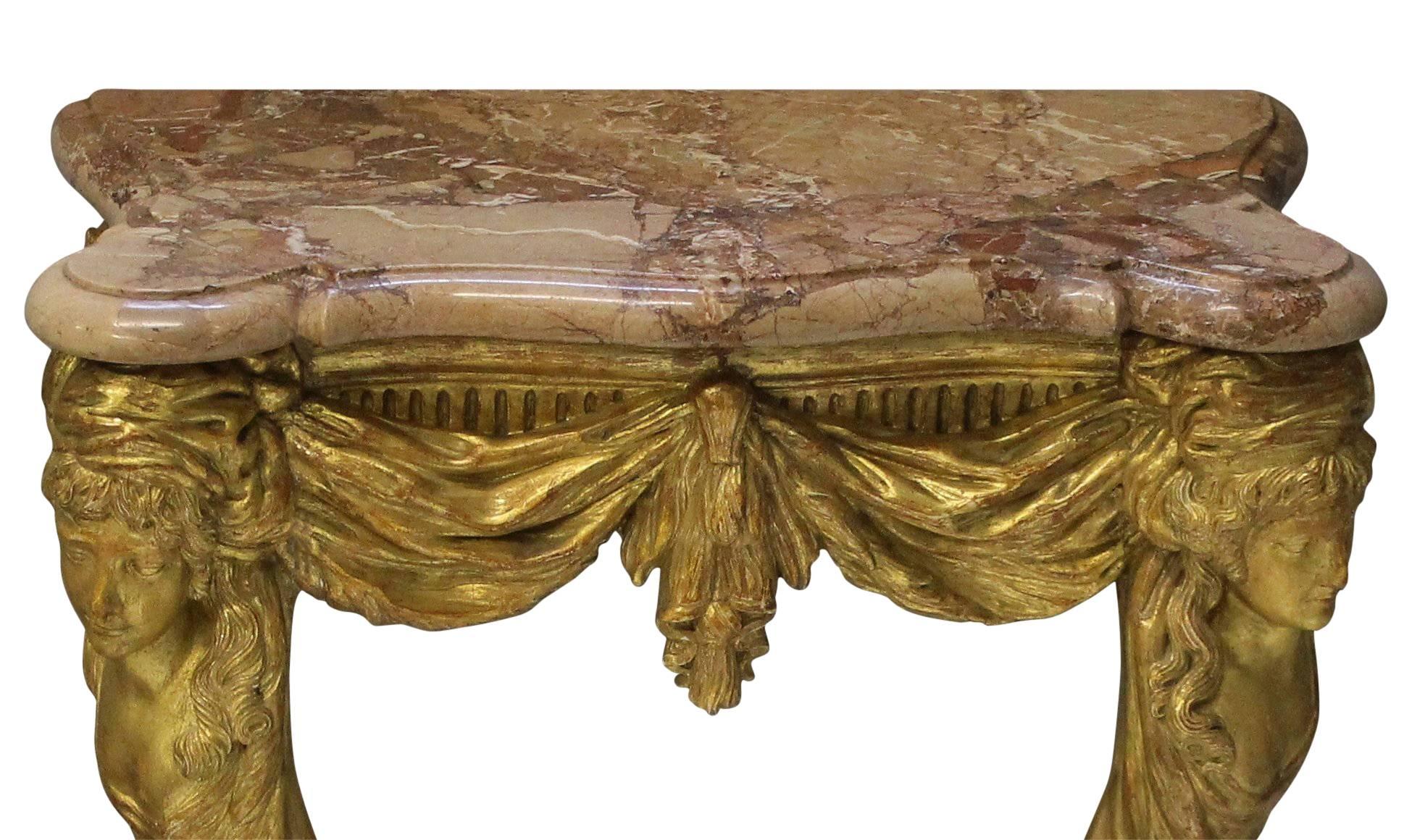 A fine English carved and water gilded console table in the manner of William Kent. The neoclassical design incorporates classical female heads and swags with goat hoof feet and a shaped marble top.
 