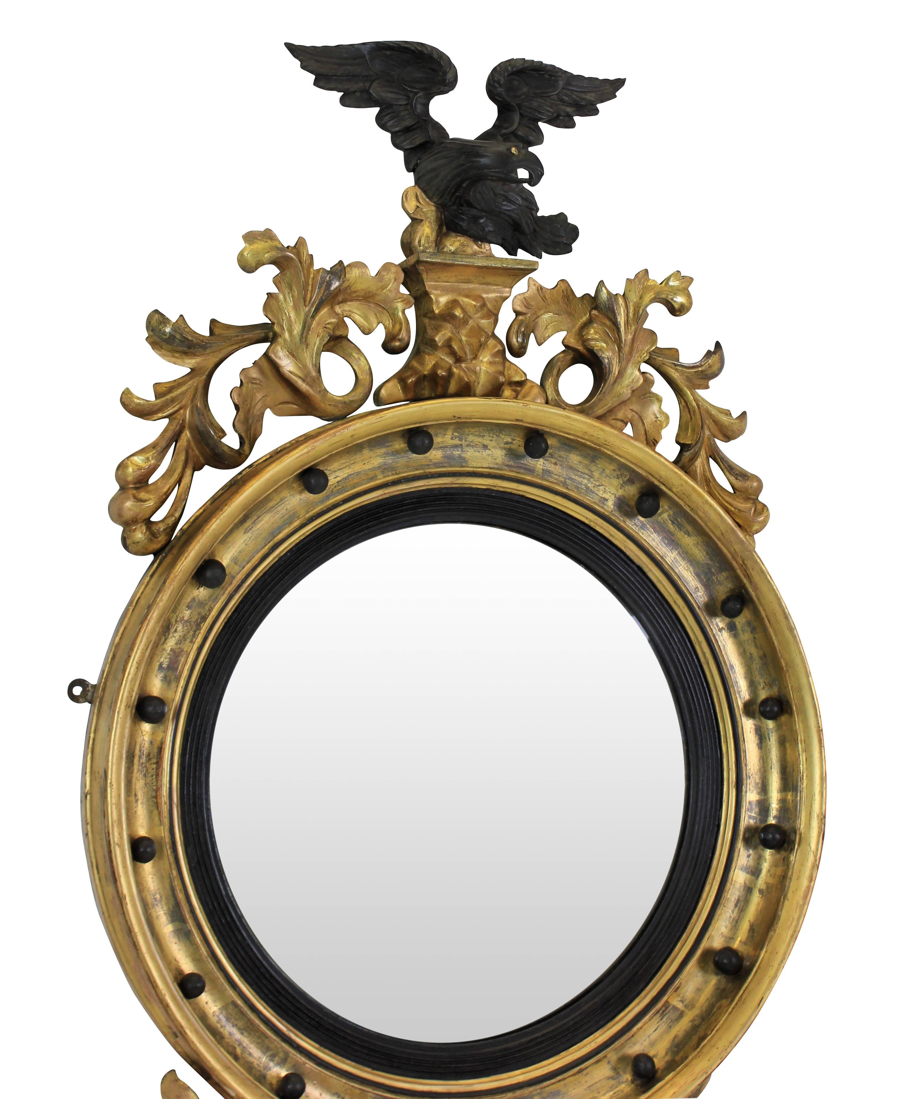 A lovely 19th century circular gilded convex mirror with ebonized slip, surmounted with An ebonized cresting carved eagle with a carved foliate apron.
 