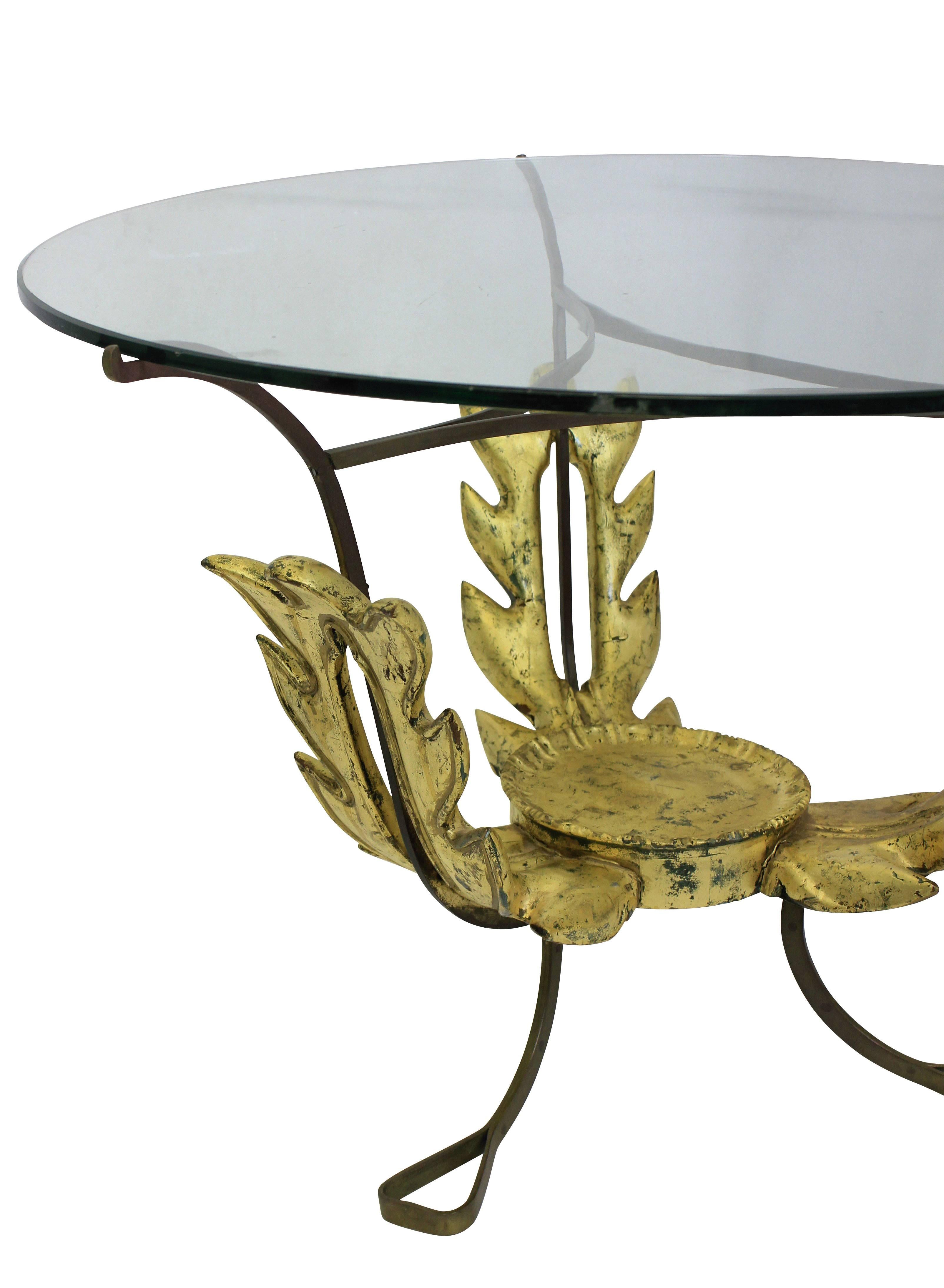 A French occasional table in brass, with carved giltwood center and a circular glass top.
 