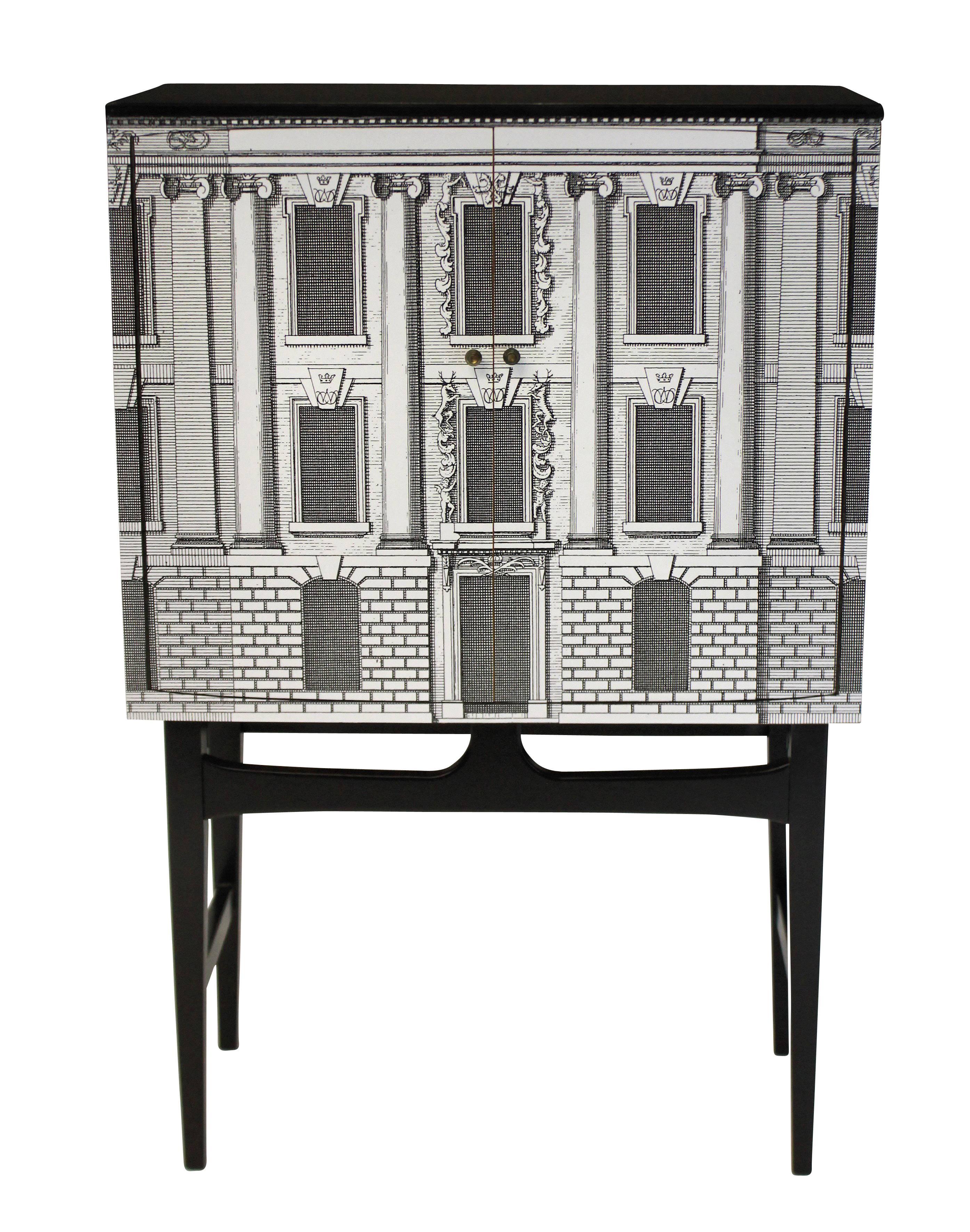 An elegant Fornasetti style bar cabinet in a Palladian design on an ebonized base, with fitted interior for bottles and glasses, with a light.
  