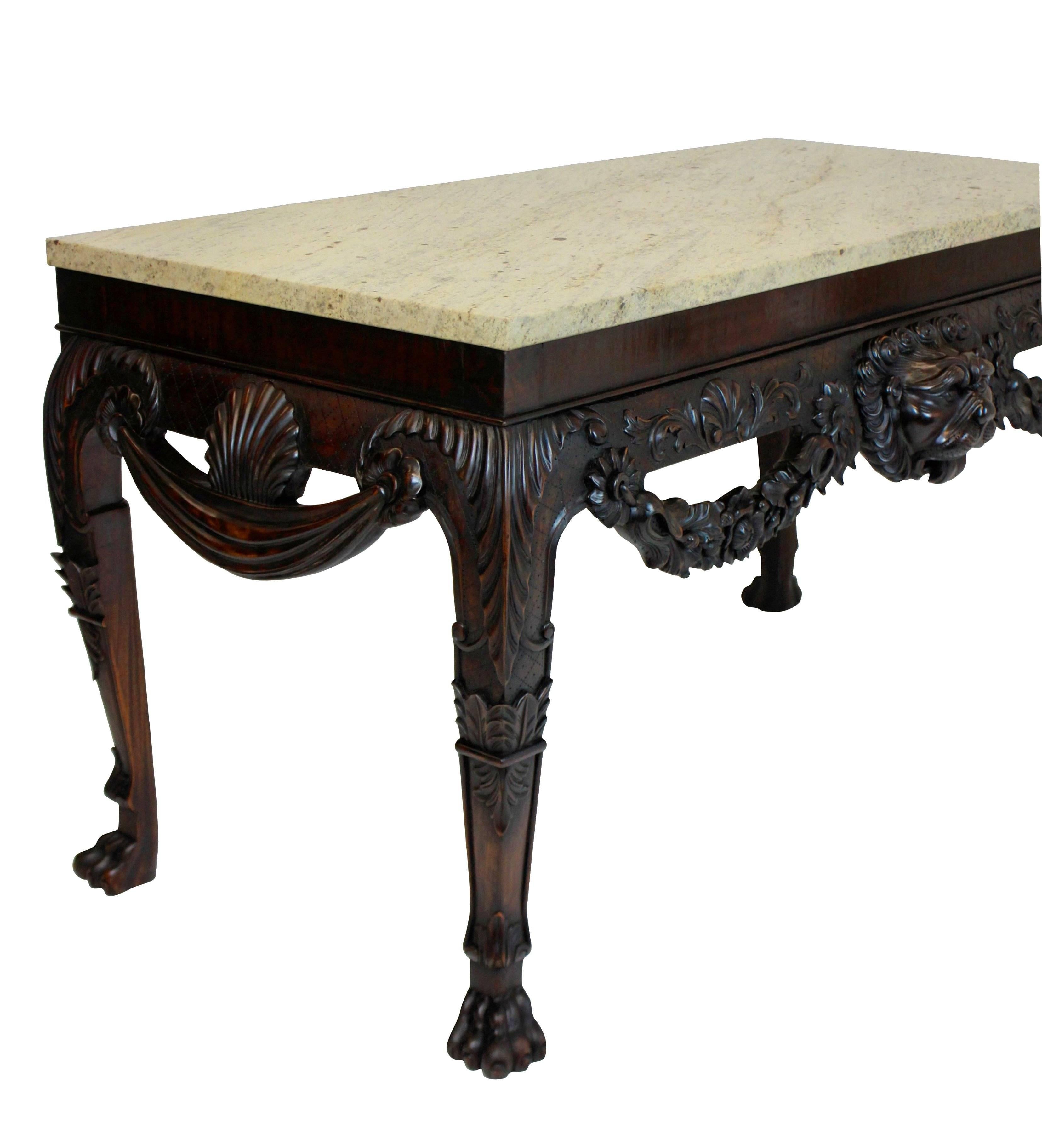 A pair of large English Country House carved mahogany console tables in the manner of William Kent of great scale and presence. The carving is well executed, with lion masks, shells and swags. The tops are honed variegated stone colored marble.

  