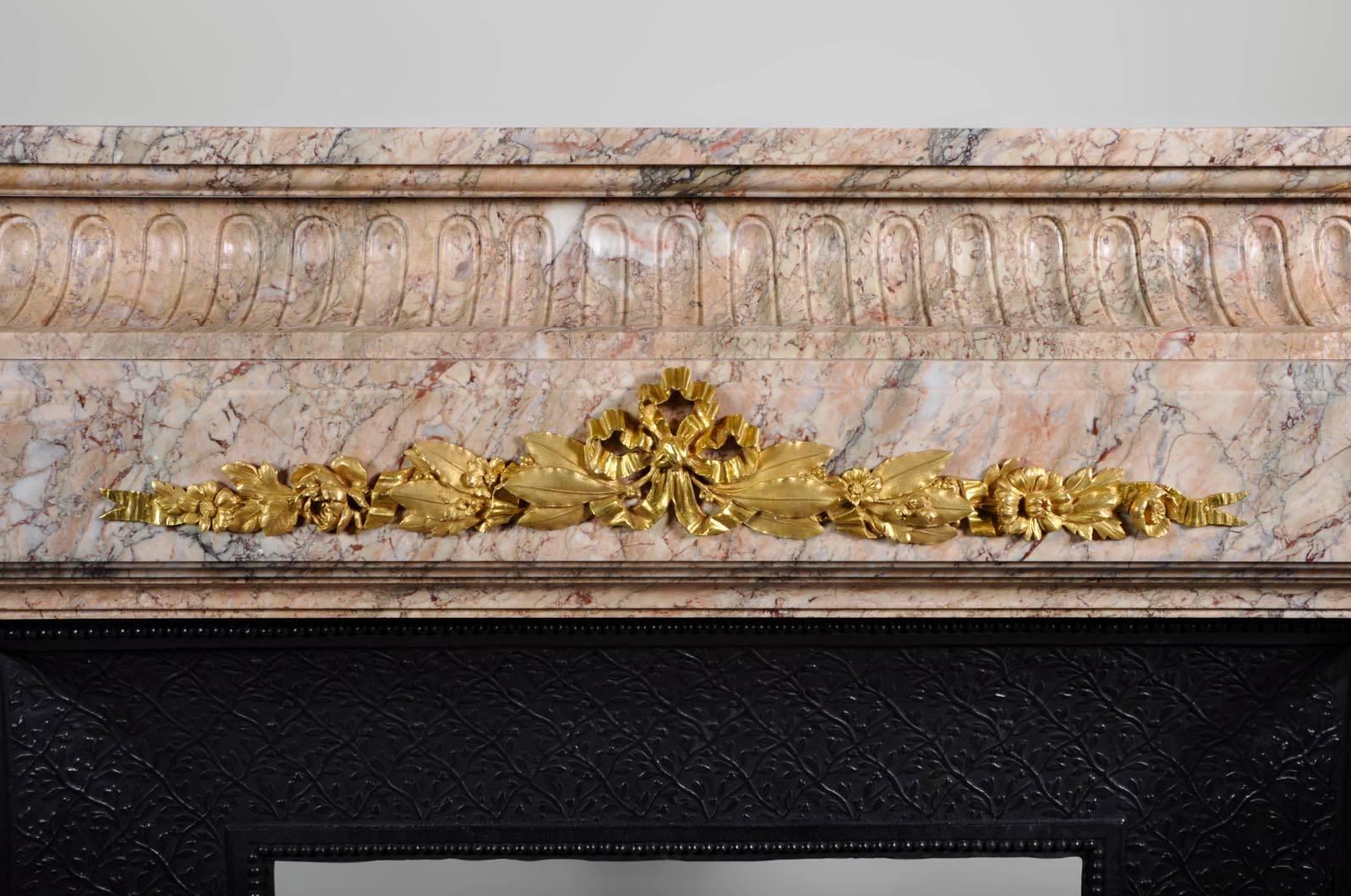 This antique Napoleon III style fireplace was sculpted in pink veined marble. The frieze and both jambs are decorated with gilded bronze ornaments representing flowers and foliages. The fireplace comes with its original cast iron insert.