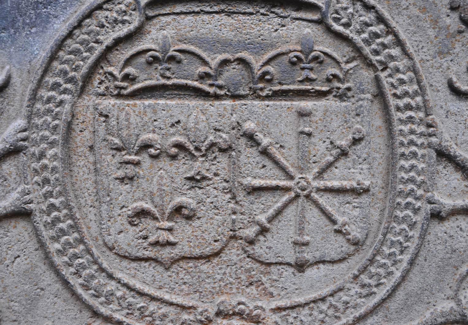This antique cast iron fireback was made in the 18th century. The France and Navarre coat of arms are represented, surrounded by two lions, in a medallion decorated with a crown.