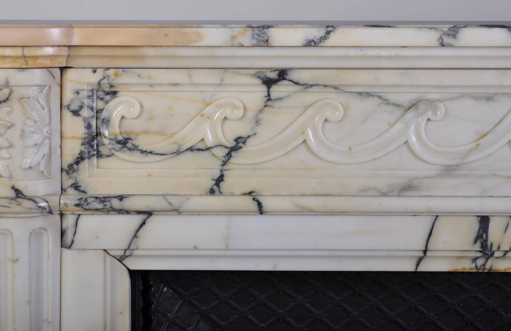 This antique Louis XVI style fireplace was sculpted out of Panazeau marble during the second half of the 19th century, in France. 
Both jambs are in form of fluted half columns with square rosettes carved in a round corner. 
The frieze is carved