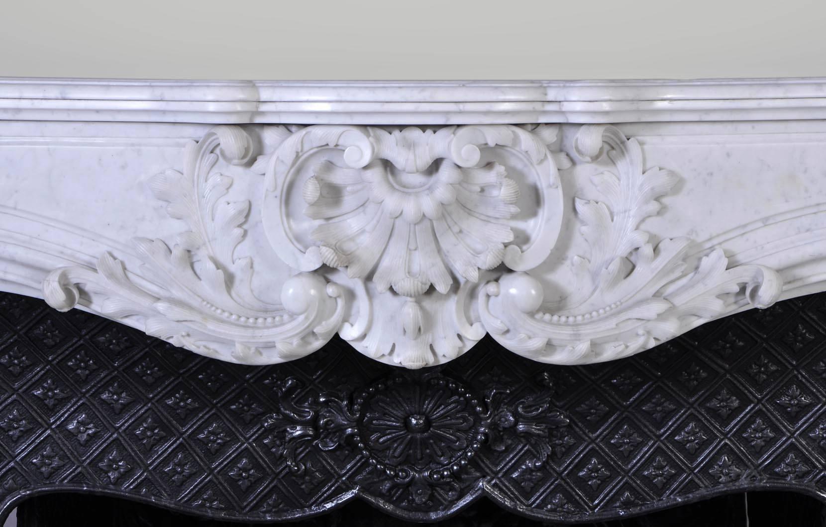 Antique Louis XV style fireplace in white Carrara marble realized during the 19th century. The opulent decor features foliaged reversed shells, acanthus leaves, medallions, scrolls. The lines are contoured and shapes are curved. 

The fireplace
