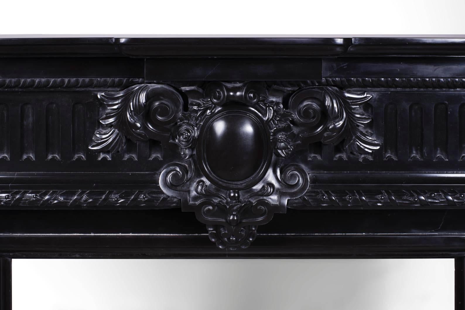 This is a rare model of large dimensions, which is very richly adorned. On the imposing jambs are carved two sculpted stands. The entablature is adorned with a medallion.
The depth of the Belgian black marble highlights the finesse of the