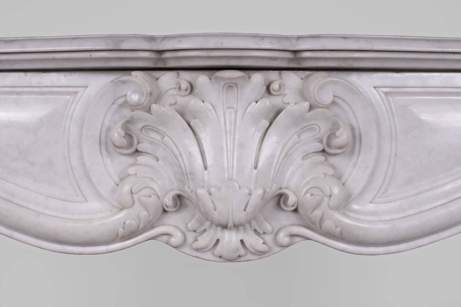 This beautiful antique Louis XV style fireplace richly decorated was made in the 19th century in a white Carrara marble. The winding jambs feature acanthus leaves at the feet and shells at the top. They support a curved frieze where medallions are