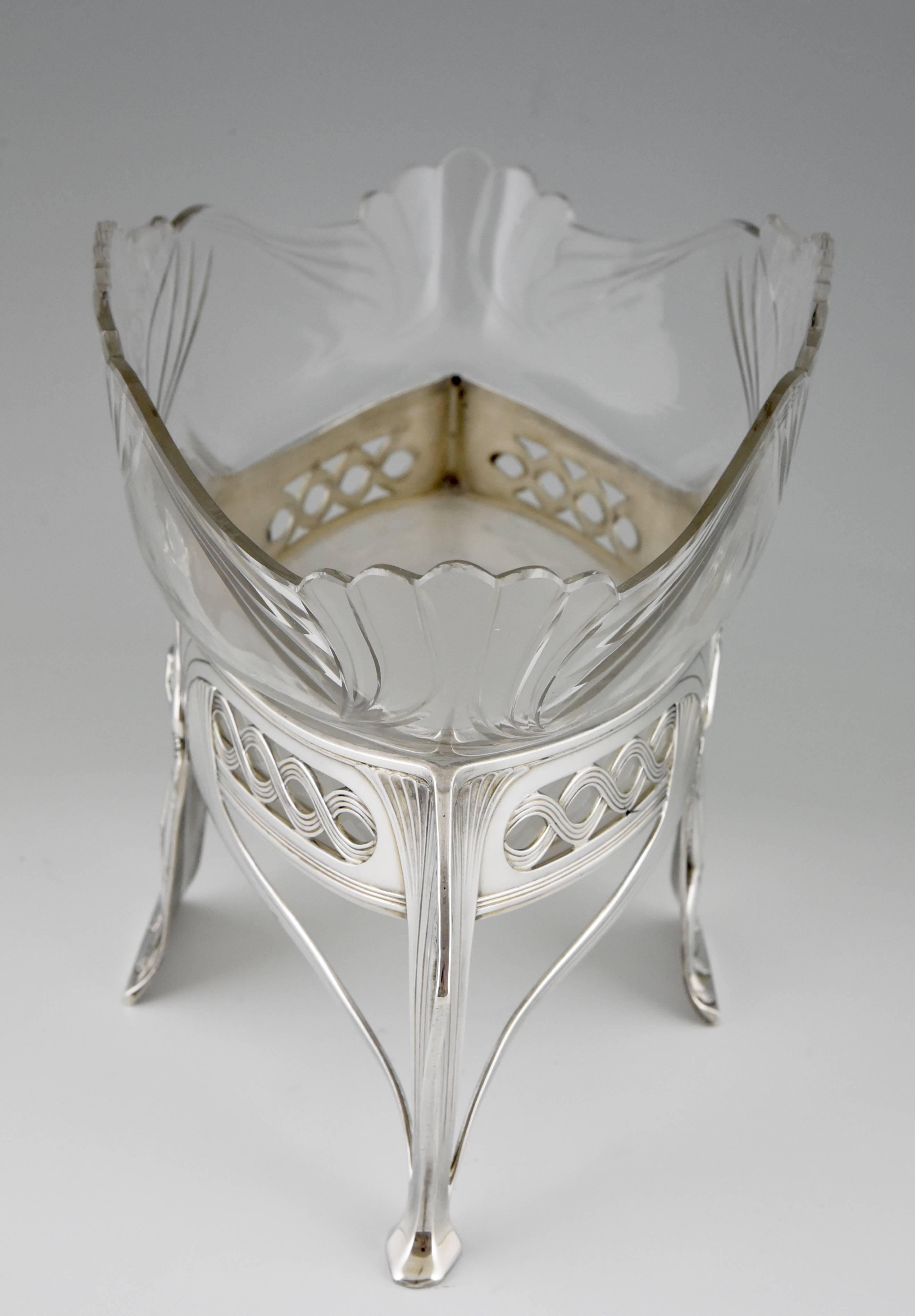 An Art Nouveau flower dish decorated with romantic semi nude couple and leaves and finely cut-glass liner.
By WMF, Württembergische Metallwaren Fabrik. 

Artist/ Maker: WMF 1906.
Signature/ Marks: WMF mark, 60, 0/1, ox, and B.
Style: Art