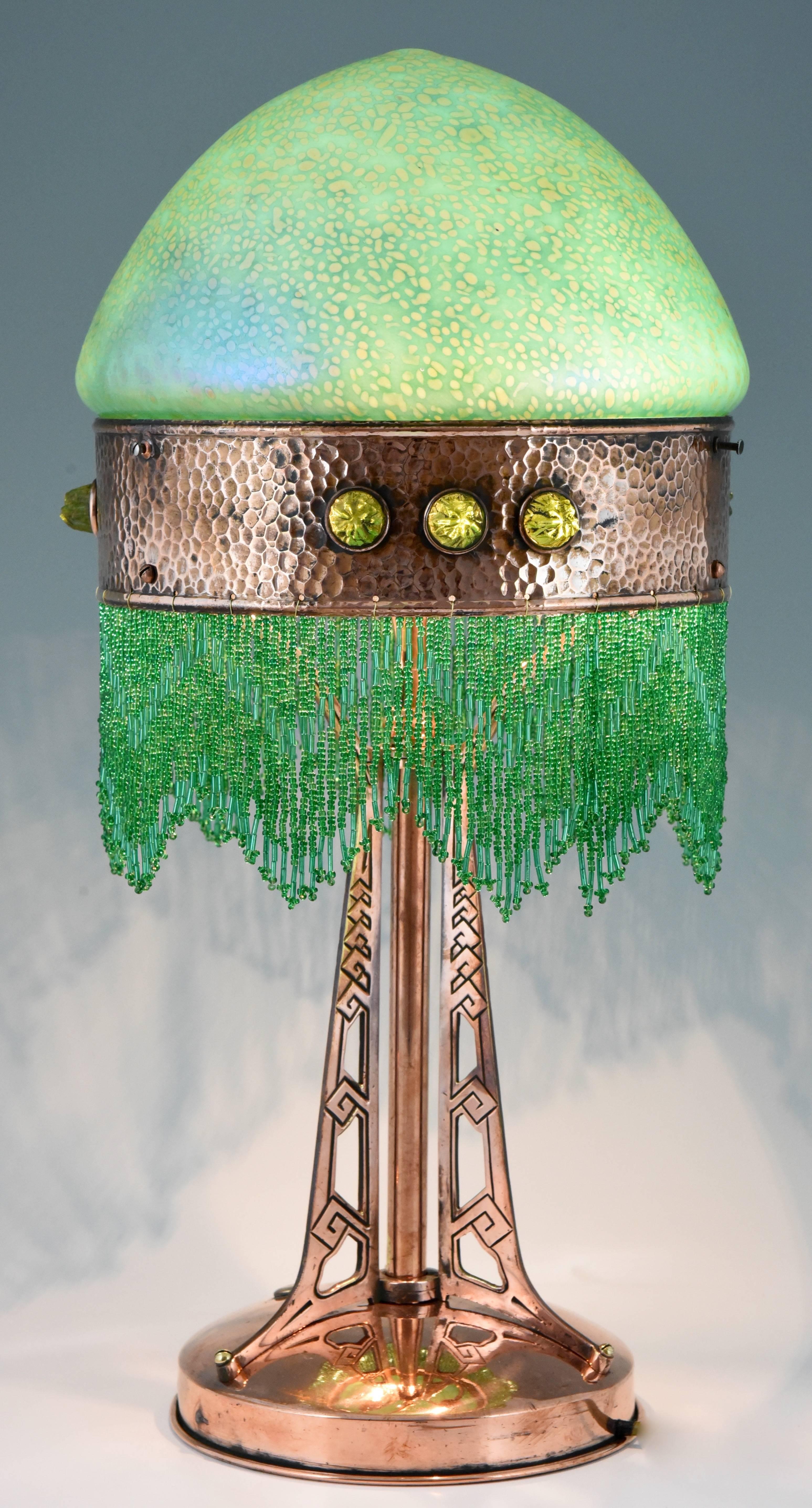 Art Nouveau Brass Table Lamp With Loetz Glass Shade and beaded fringe. 

Artist/ Maker: Johann Loetz, Witwe.
Style: Art Nouveau.
Date: 1900-1910.
Material: Iridescent glass and copper.
Origin: Austria
Size: H. 53 cm x L. 26 cm. x W. 26 cm.   
H.