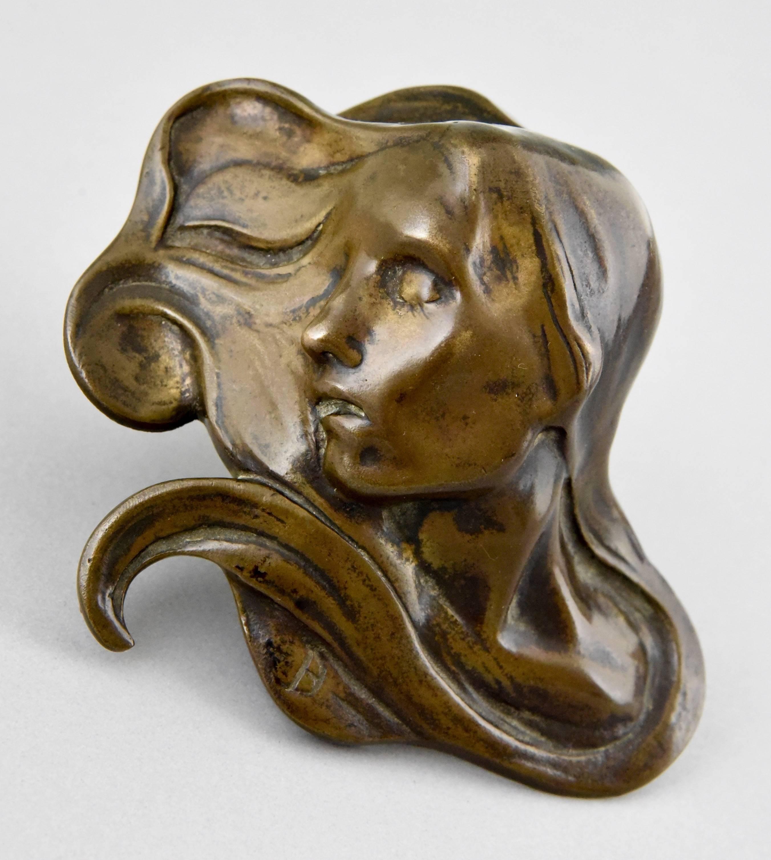 A paperweight in the shape of a females face with swirling hair.
By Paul Dubois.
Artist/ Maker: Paul Dubois.
Signature/ Marks: Monogram PD.
Style: Art Nouveau.
Date: 1900.
Material: Bronze.
Origin: Belgium.
Size: H 4.5 cm x L 11.5 cm. x W