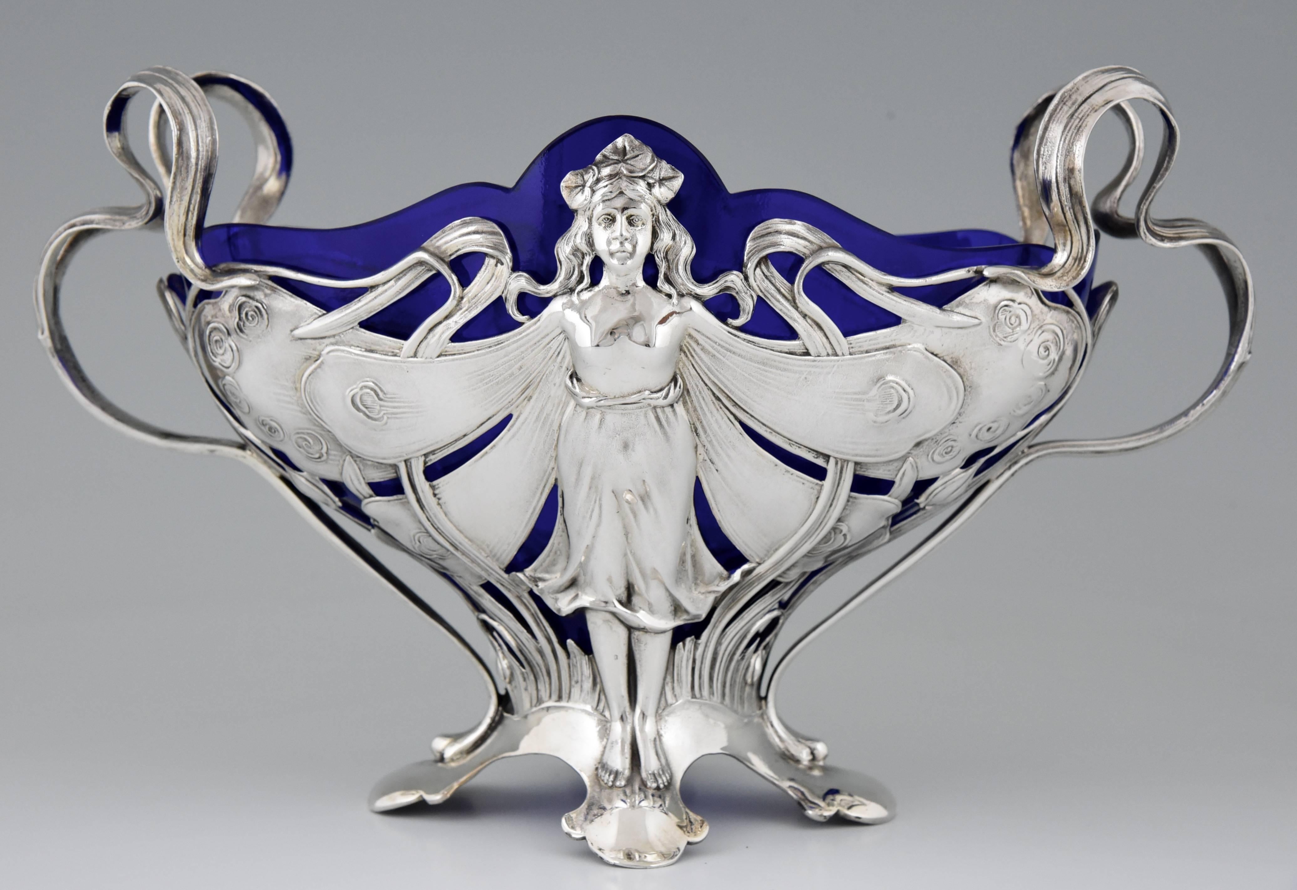 An Art Nouveau flower dish with butterfly lady and blue glass liner.

Stamped WMF mark, 0/1 and B. 

A picture of this model is shown on page xli of the book
”Art nouveau domestic metalwork from Württembergische Metallwaren Fabrik 1906”