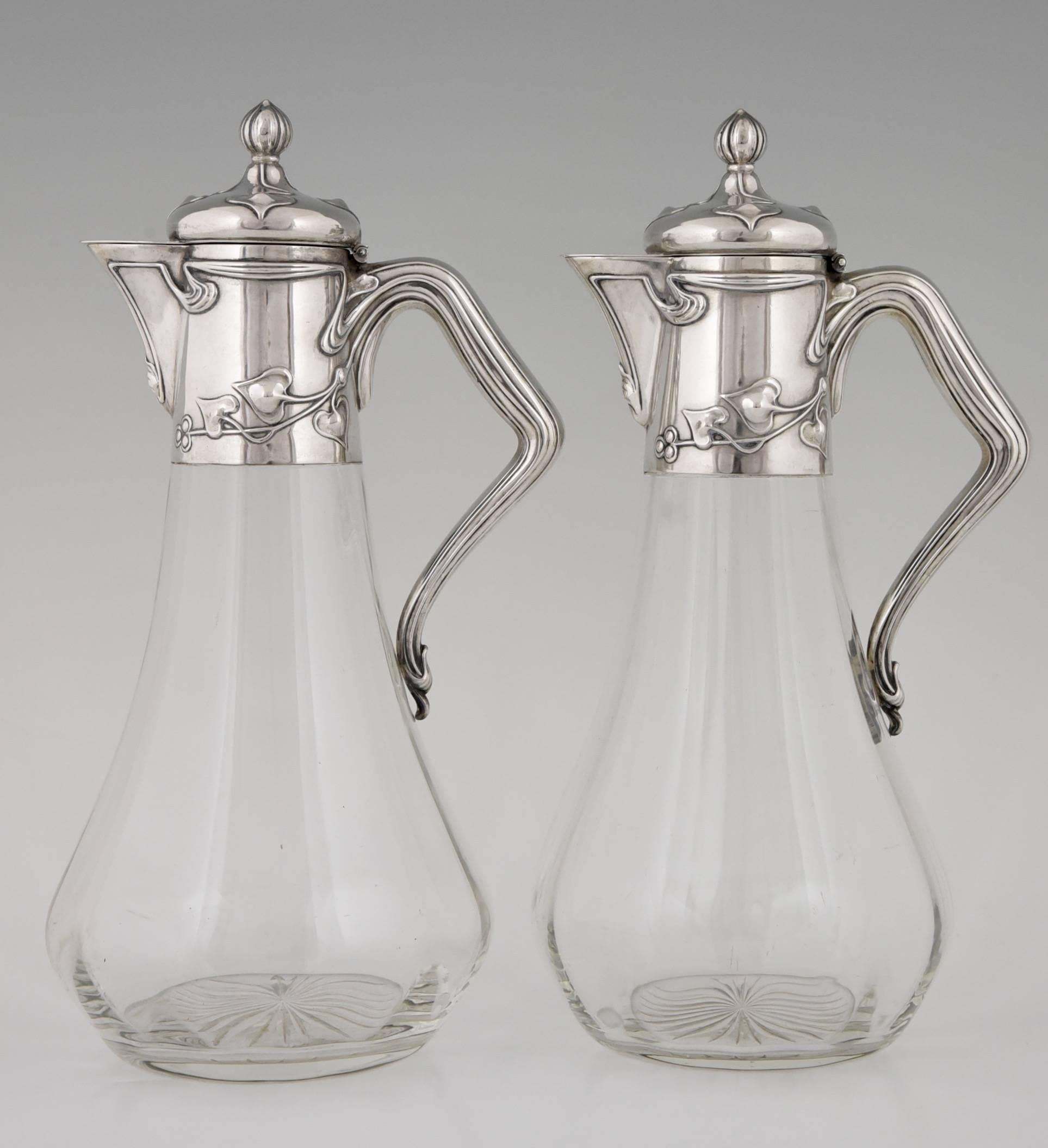 A pair of Art Nouveau silver and glass wine decanters with floral design on mount and handle.
Marked: 
Koch & Bergfeld mark 800
Moon and crown.
Number.
Frey und Söhne (Jeweler where the decanters were sold around 1900)

Literature:
Art