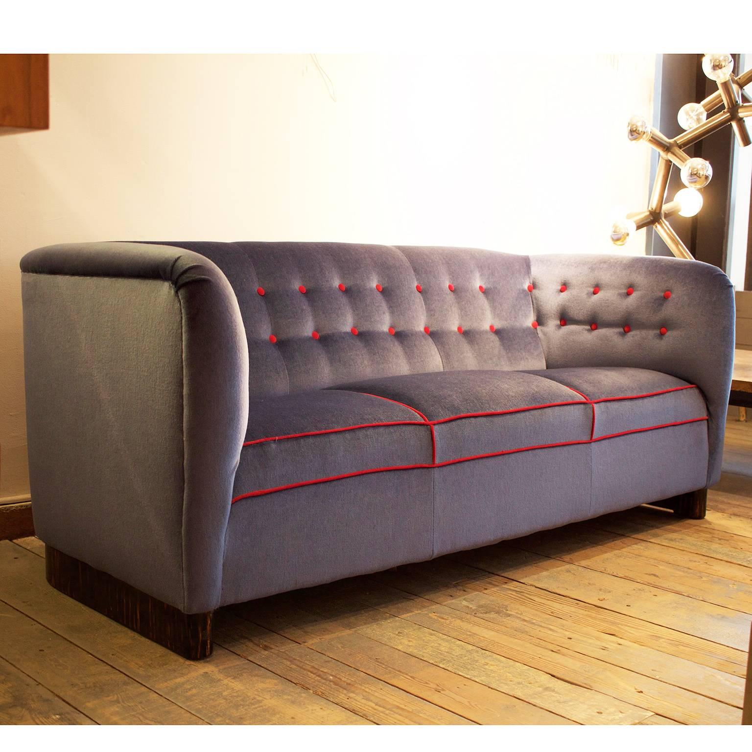 Three-seat sofa with plinth of dark stained beech upholstered with blue velvet fabric and red velvet piping and tufting buttons.

Manufactured by Fritz Hansen.