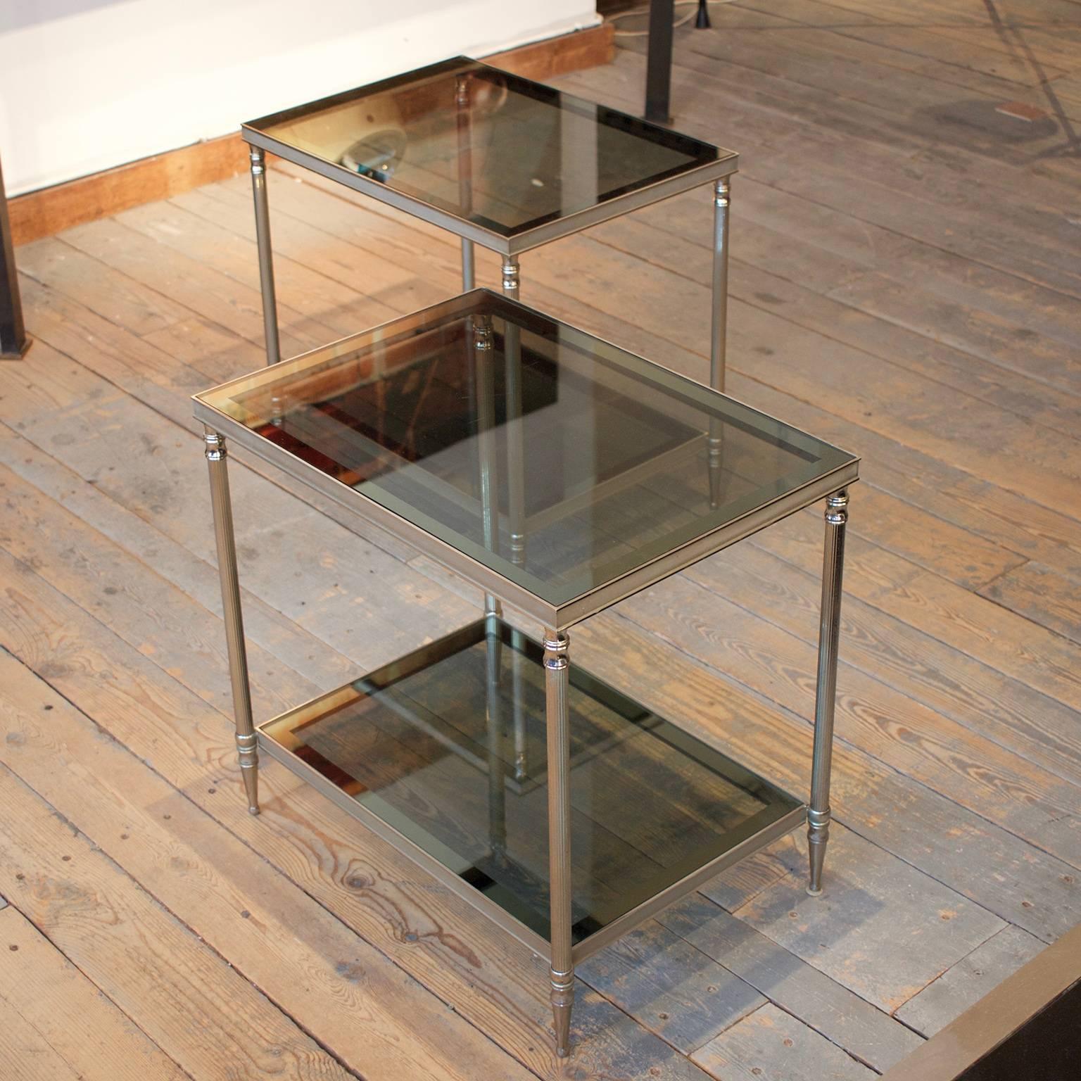 This pair of French end tables, nickel-plated brass, in neoclassical style has fluted legs. Two levels of smoked glass complete the look. 

A versatile piece that blends well with both contemporary and traditional interiors.