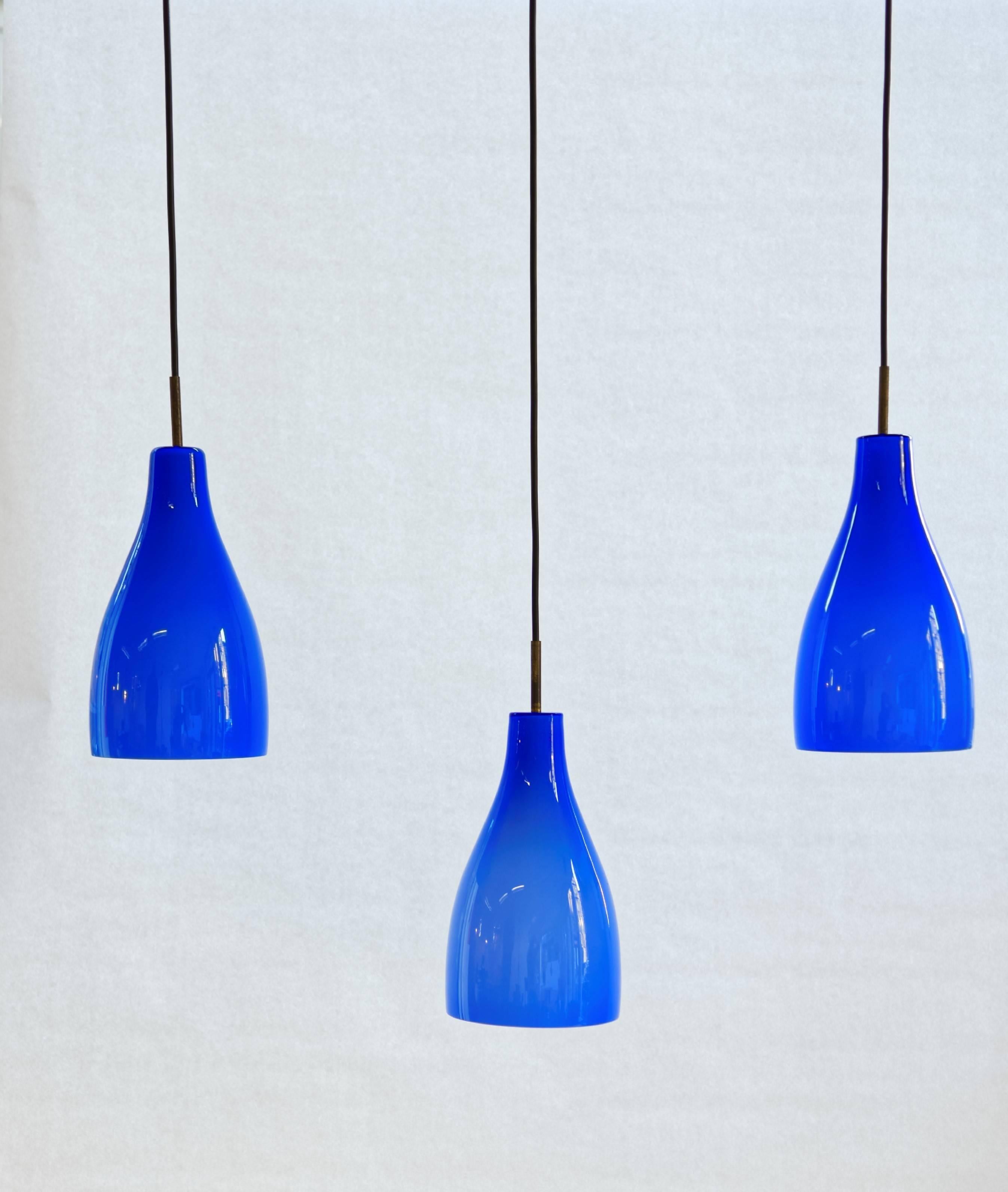 Set of three pendants designed by Massimo Vignelli (1931-2014) and executed by Venini, glassworks in Murano, Italy.
Transparent royal blue glass on an inner white opaque glass. Brass frame. One light bulb by lamp.