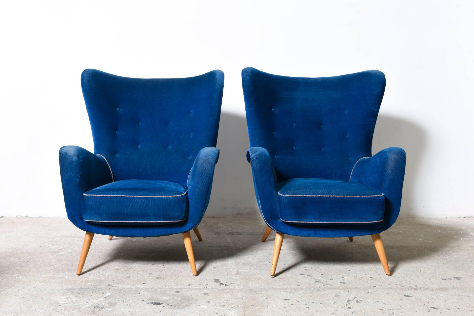 A rare pair of Mid-Century oversized lounge chairs each with a well-shaped backrest with wing detail and armrests.
The clubs also feature round tapering beech legs

Organic shaped blue velvet cocoon lounge chairs features its original upholstery.