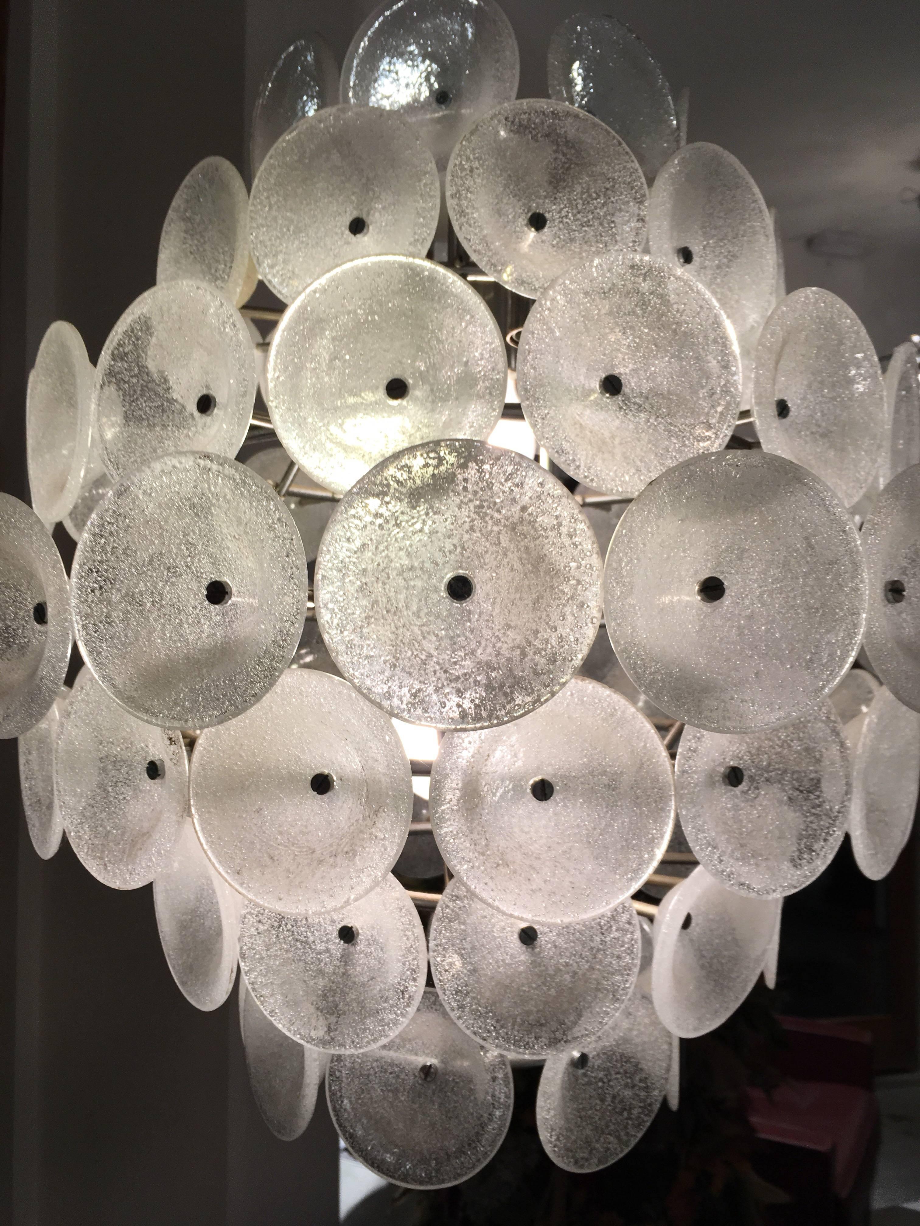 A Murano Chandelier with seven tiers of solid blown glass with air bubbles textured discs attached to a metal chrome base frame to make up this ultra-mod looking chandelier. 
Its compact size is a great look,great installed as a pendant in spaces