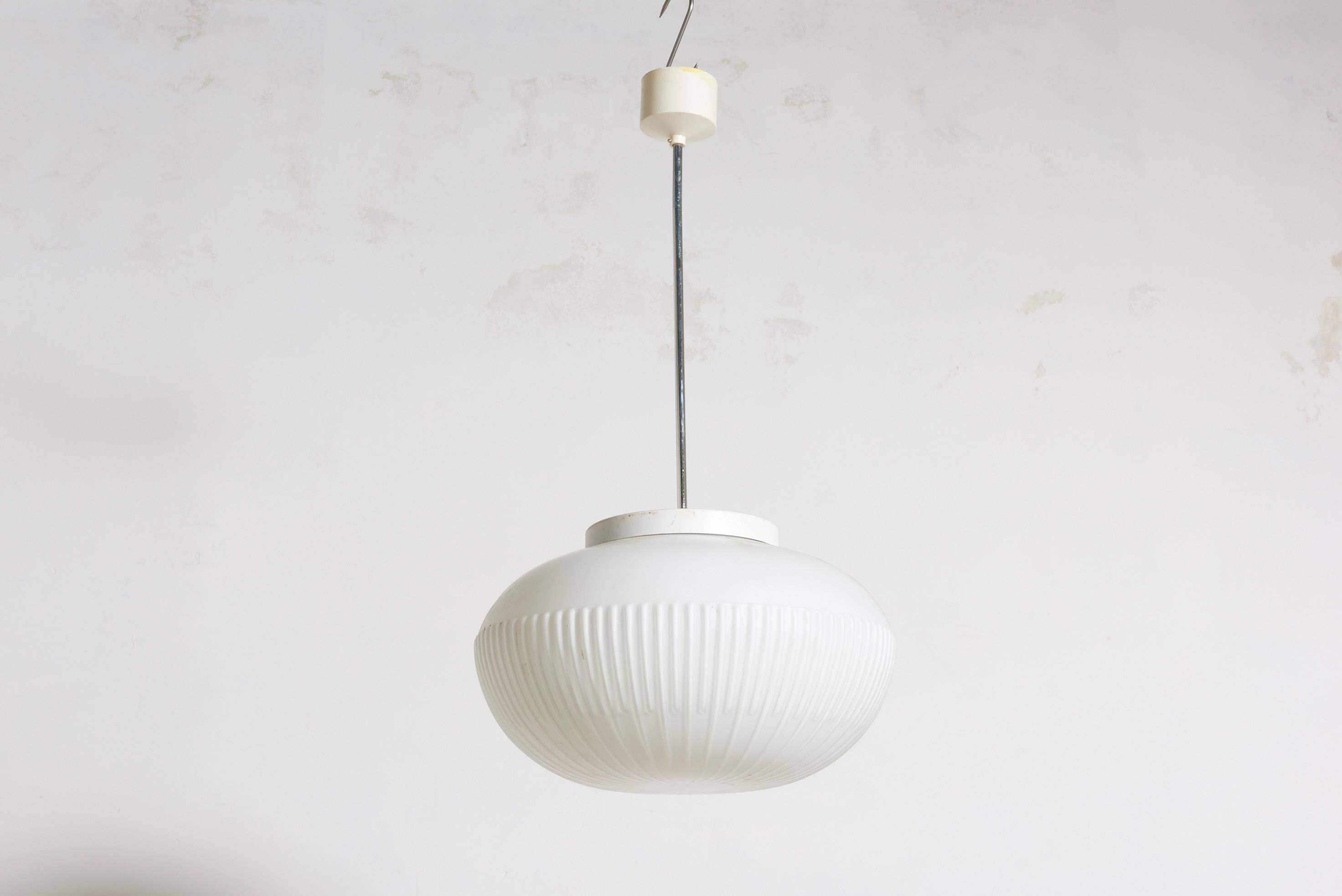 Bellissimo pendente in vetro opalino con strisce in rilievo che dona un effetto di luce molto bello nel tuo ufficio o nel tuo soggiorno; il sistema di sospensione è un tubo cromato con una parte superiore in bachelite. Otto pezzi disponibili.
