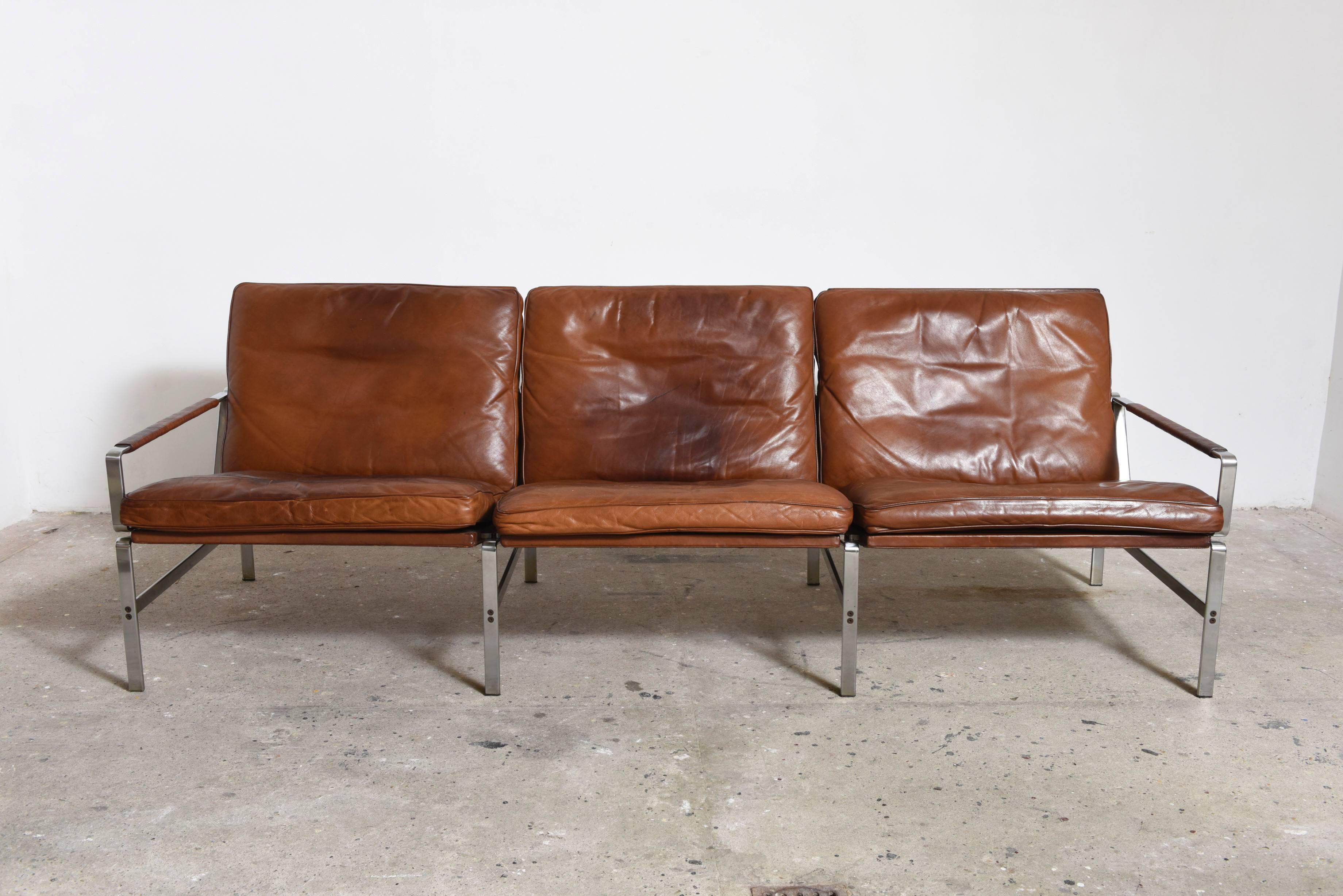 Preben Fabricius & Jørgen Kastholm for Kill three-seater sofa model FK6720 designed in 1968 in chromed steel,upholstered with brown cognac leather 
cushions,armrest wrapped in rattan. 
L.215 cm.Minor wear consistent with age and use,one cushion