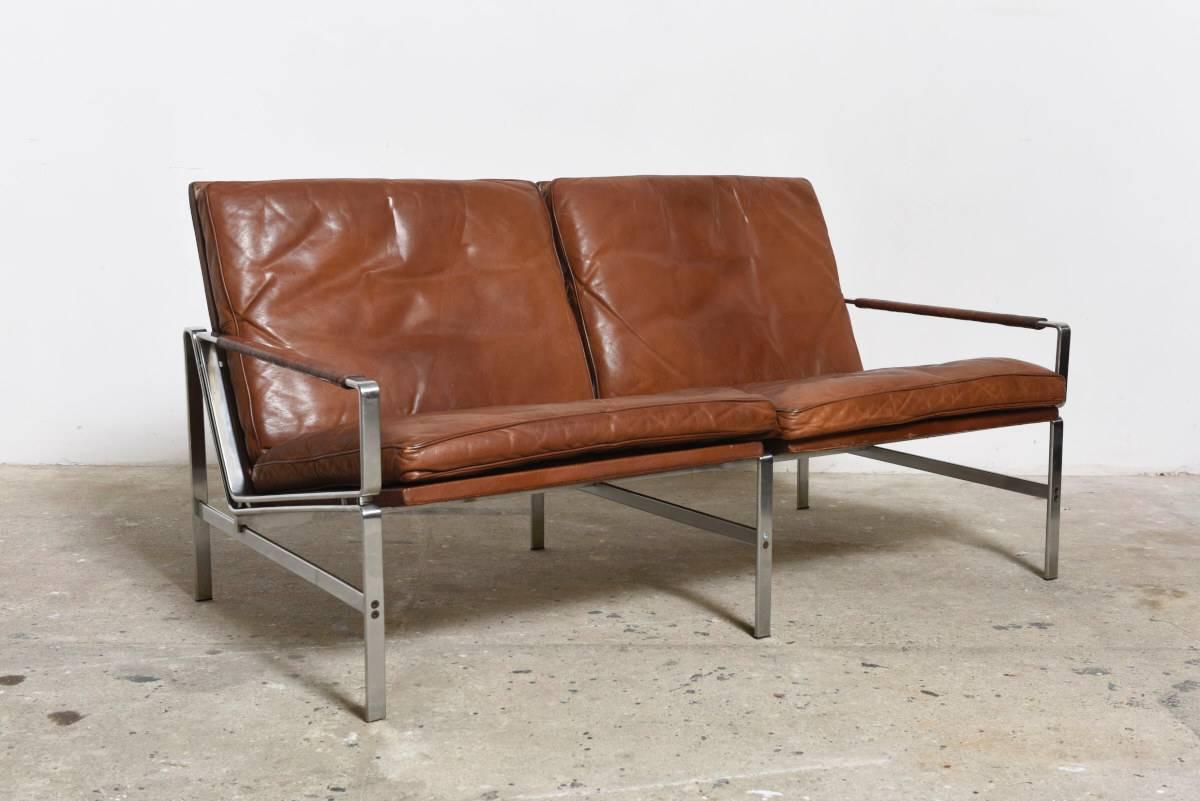 Two-seat sofa FK 6720 by Fabricius & Kastholm, 1967.
Made by Kill International, Germany.

Cognac brown leather with naturel patina and chromed steel frame,
the armrests are wrapped with natural rattan.

Got a matching with two lounge