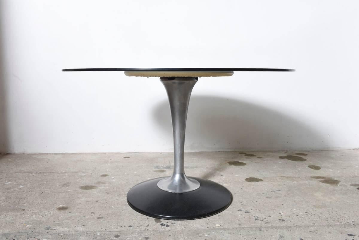 This round dining table is composed of a smoked glass top and a polished chrome tulip base. 

It's a simple but very striking design that creates the effect of spaciousness, with the quality of the chrome and the transparency of the glass.