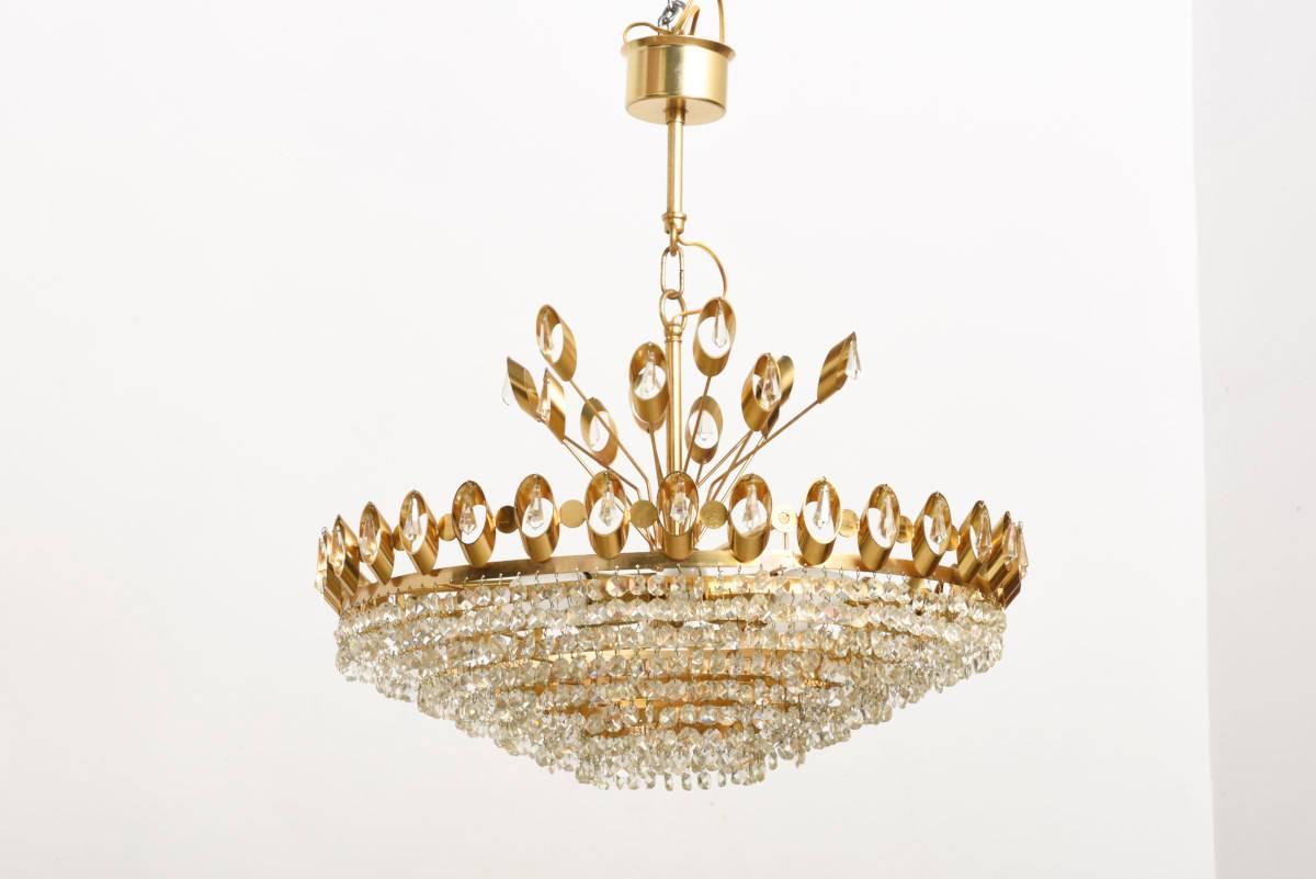 Hollywood Regency chandelier from Palwa. 
The chandelier has a 24-karat gilt brass frame with wonderful faceted crystal glass beads which lights up every room in a beautiful warm light. 
It is fitted with six E14 bulbs.
Set of two chandeliers