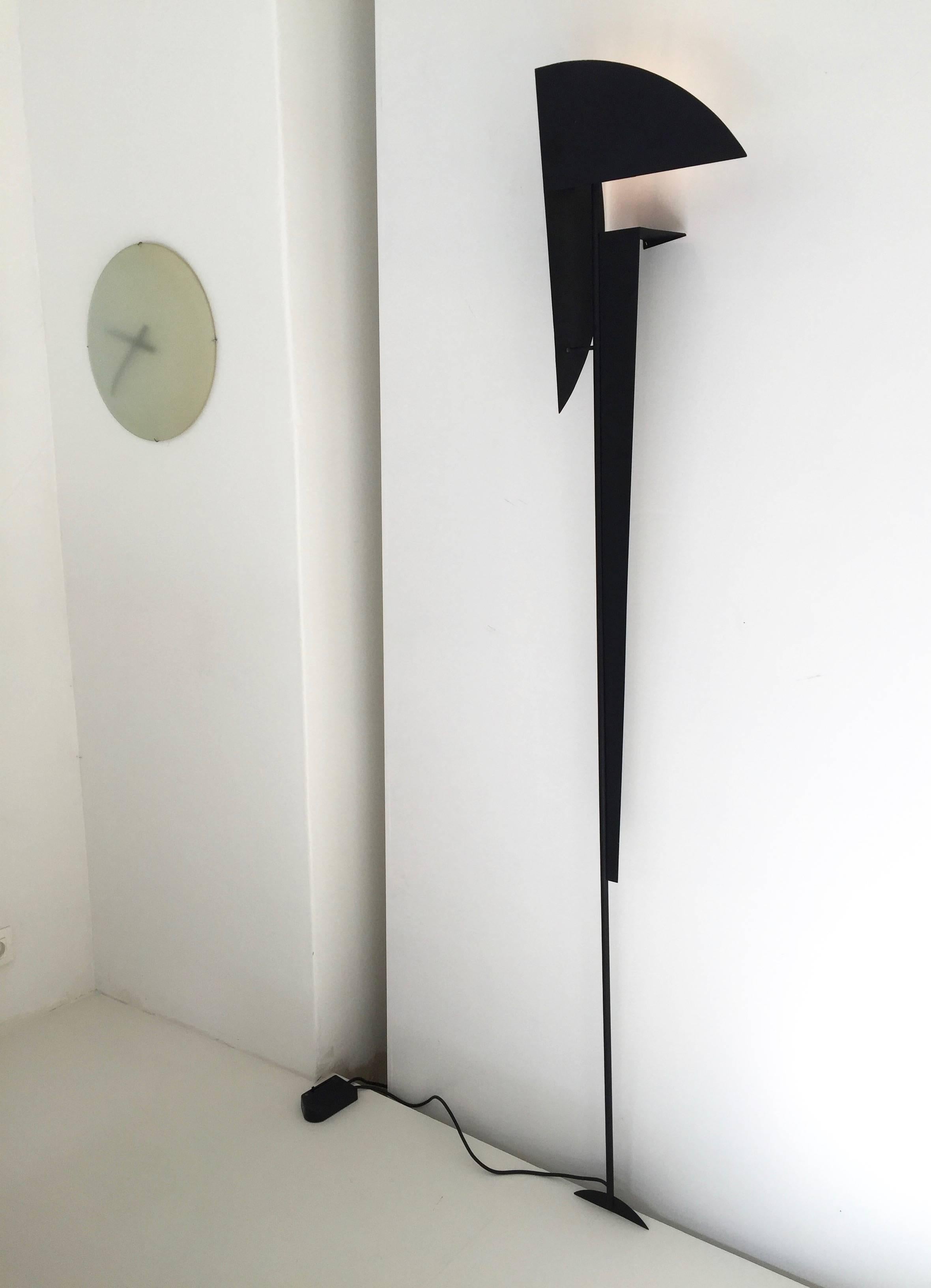 Unusual anonymous lamp sculpture attached against the wall and resting on the floor. It has a constructivist or abstract figurative approach. It is made in thin lacquered metal and has a normal light bulb as light source which is disable with a foot