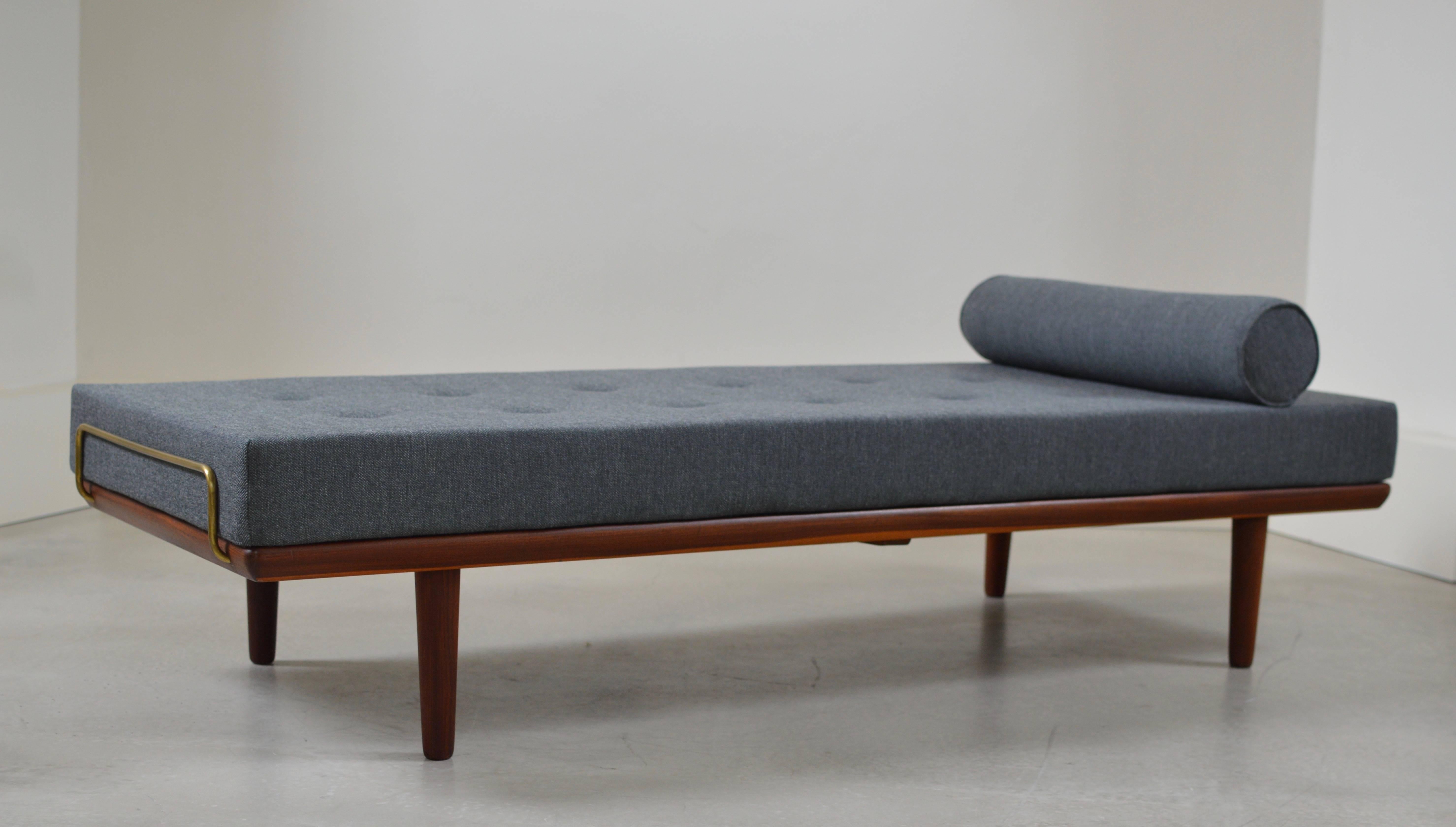 Daybed model GE19 from 1956 constructed from solid teak with beautiful contrasting brass mattress support bars on both sides. 
The daybed comes with a completely new mattress and neck roll pillow executed with a high end dark grey fabric (mainly