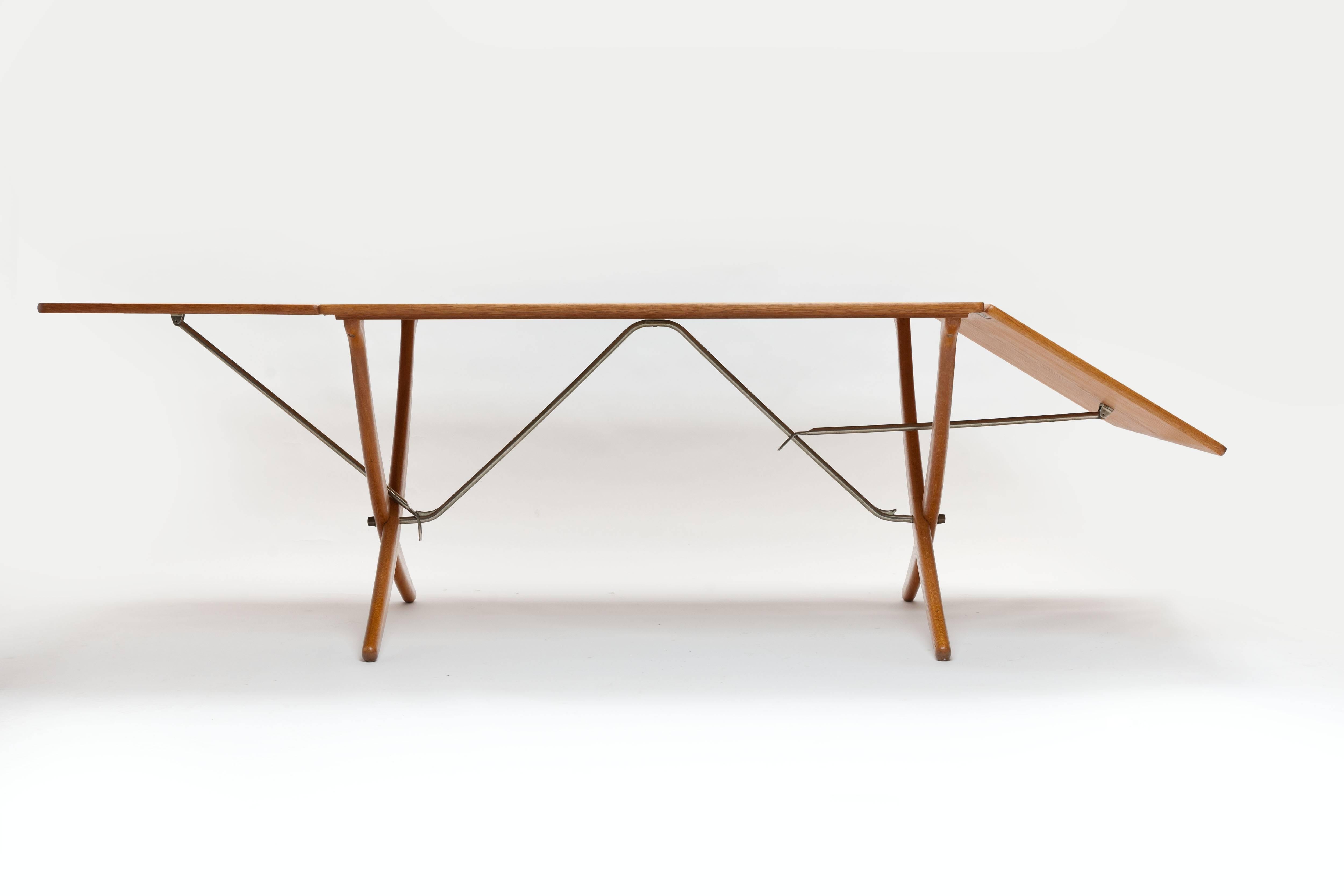 Hans J. Wegner oak dining table model AT-304 with two flip-down leaves and sabre cross-legs with brass stretchers, manufactured by Danish cabinetmaker Andreas Tuck (signed with burn mark). 
A striking and multifunctional dining table that also