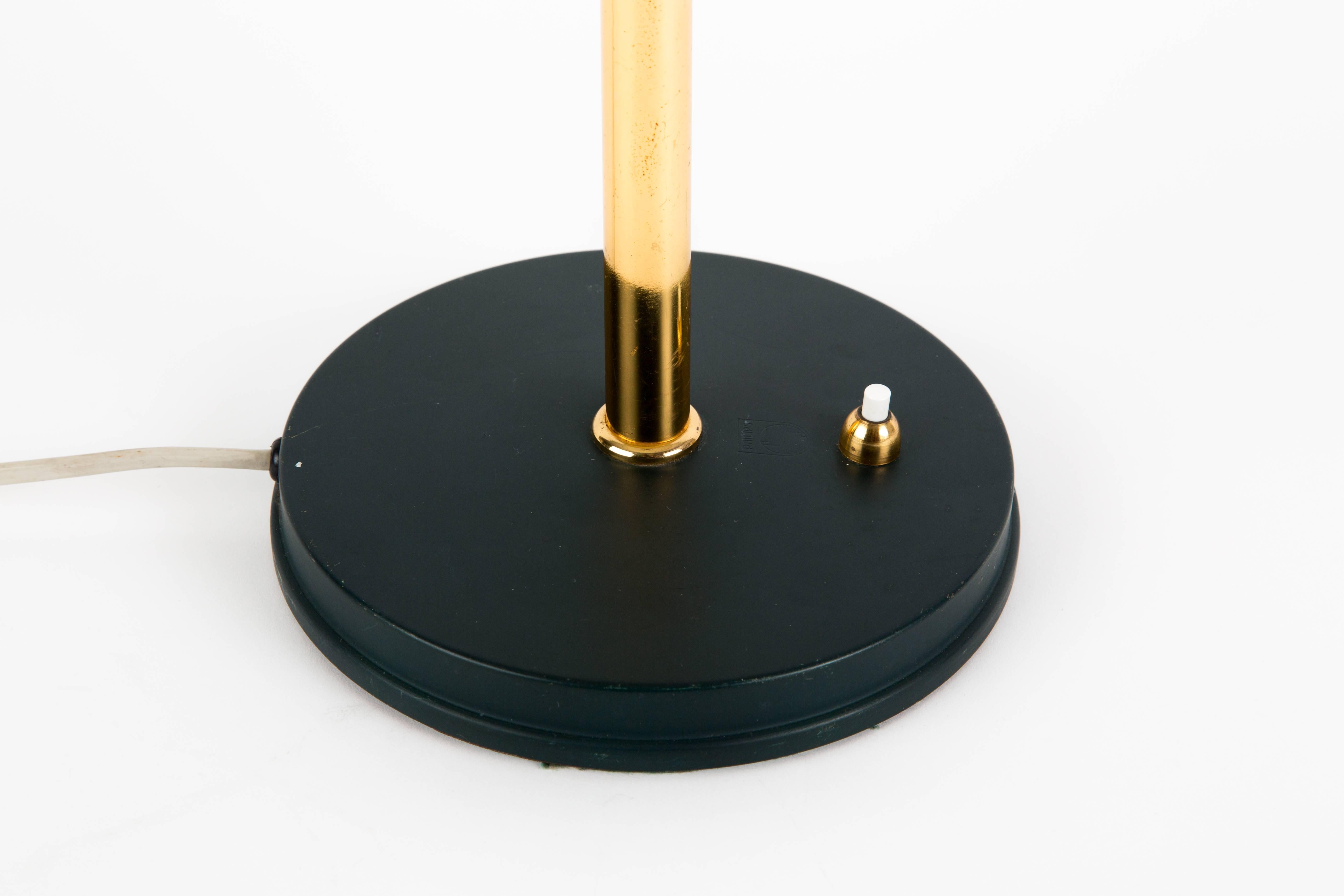 Table lamp designed by Louis Kalff for Philips. The dark green hat has a hole on the top. This is a lovely detail for the light effect. The standard is of brass. The switch is also with a brass ring, very nice eye catcher.