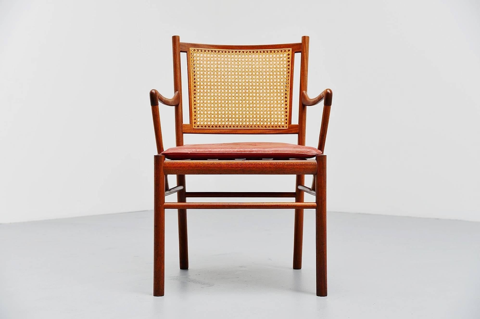 Very nice Colonial armchair designed by Ole Wanscher, produced by Poul Jeppesens, Denmark, 1960. The chair has a solid teak wooden frame and a cane back. It still has its original red leather seat which has a nice patina to it and some craquele (see